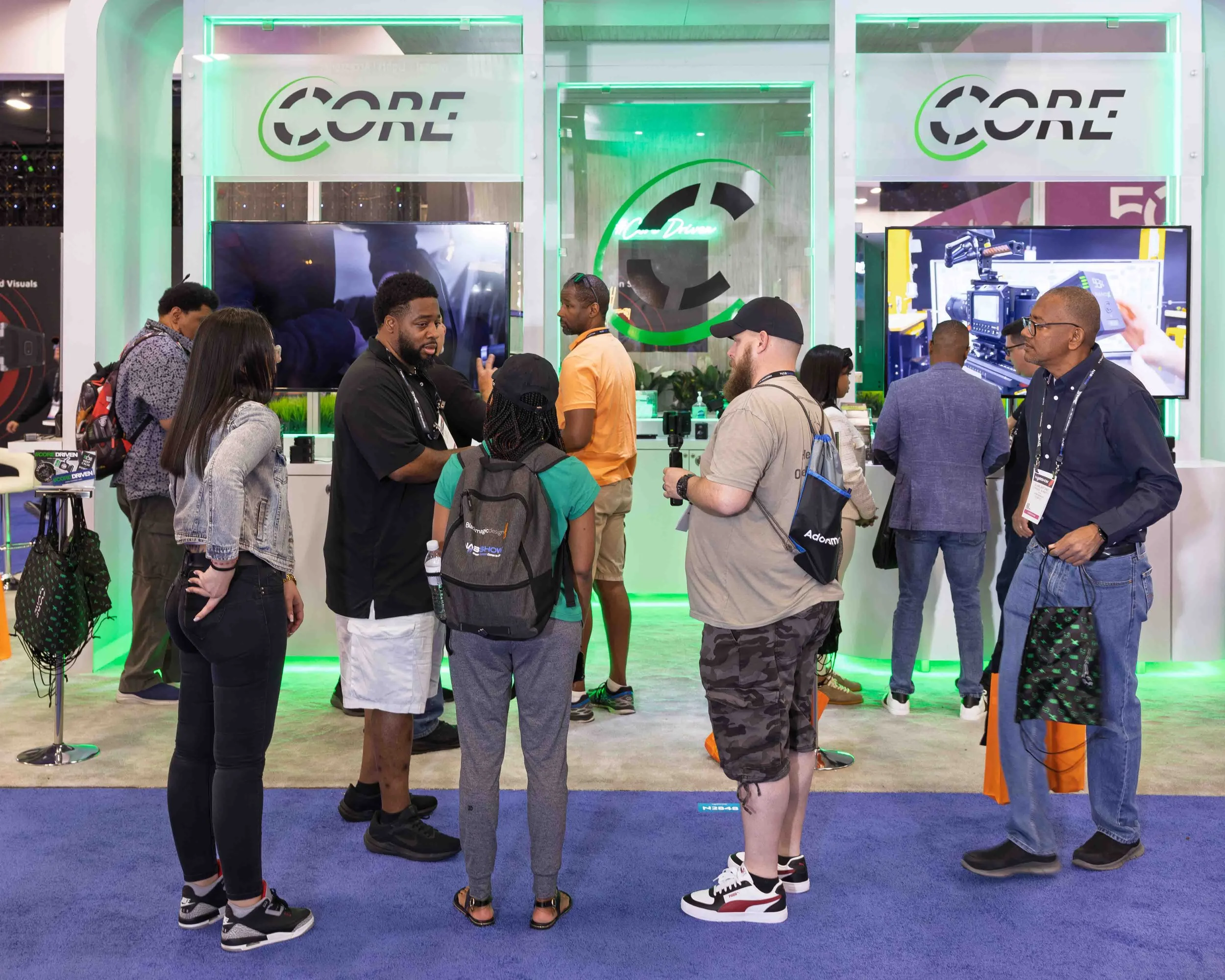 People talking at a corporate event conference trade show booth with the logo 'CORE' displayed above, featuring large screens and technology products.