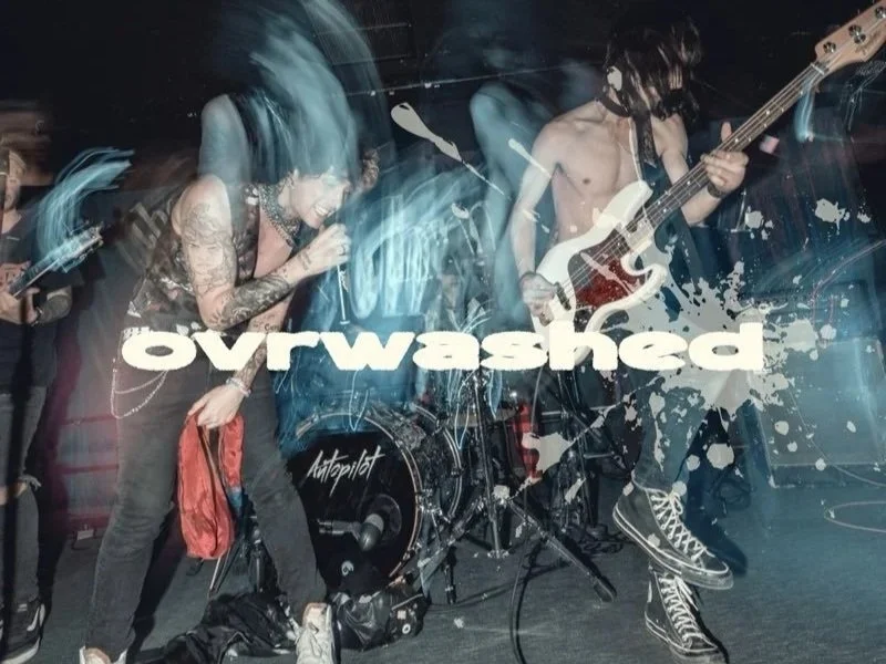 A band performing live on stage with a female vocalist and a male bassist, with the word 'overwashed' in bold letters across the image and a splatter design.