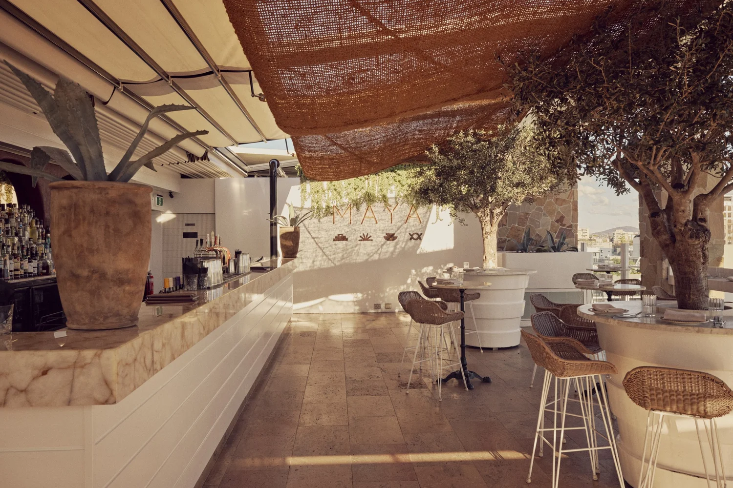 The main bar at MAYA with its marble counter, bar stools and olive trees