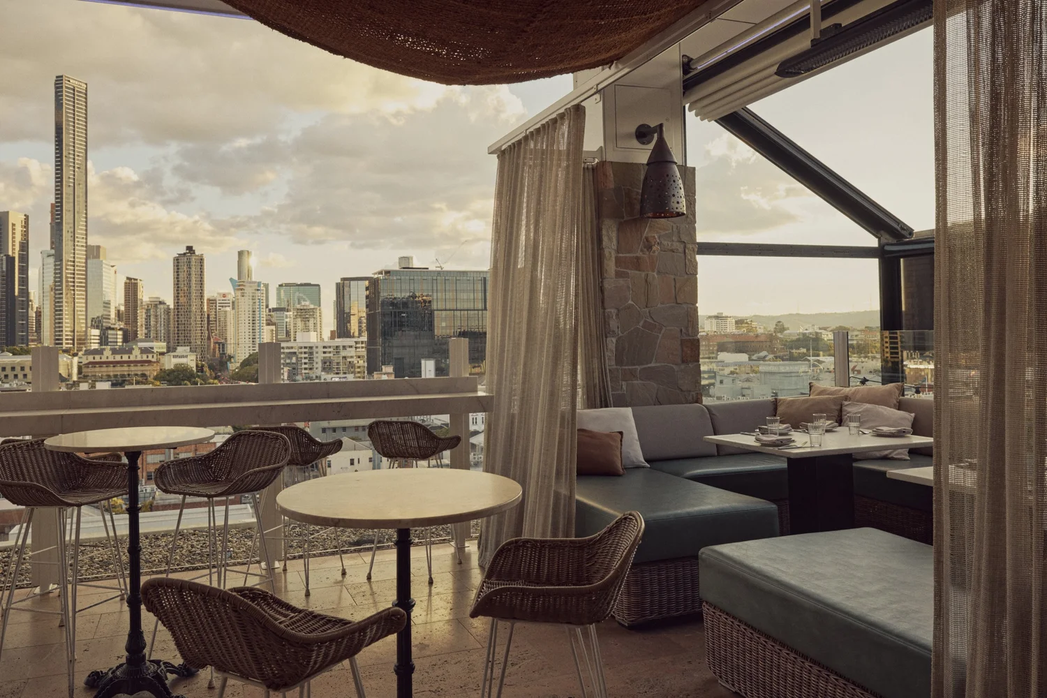 High tables and lounge booths at MAYA facing the Brisbane skyline at sunset