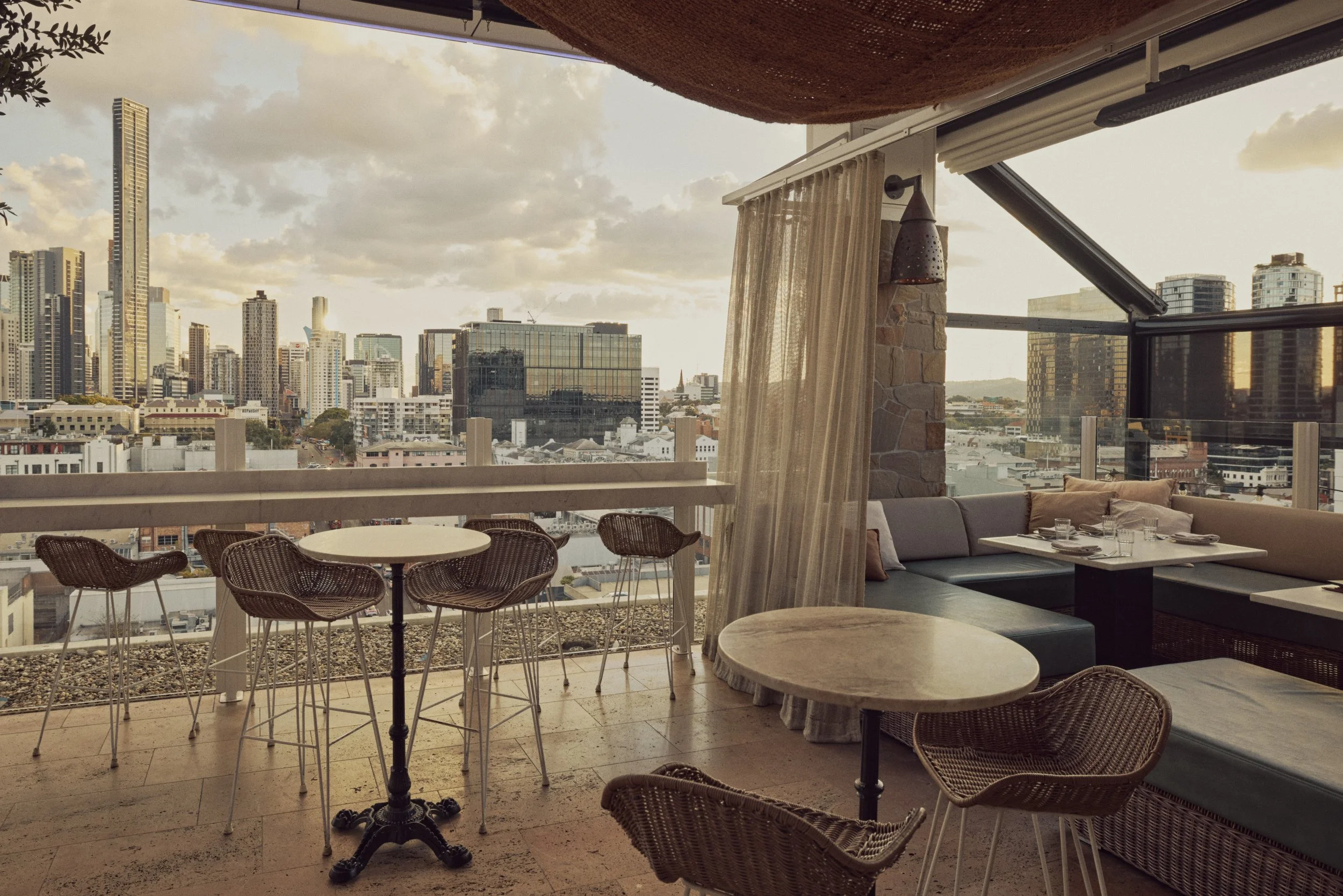 MAYA rooftop at golden hour with high tables, lounge booths and the Brisbane city skyline