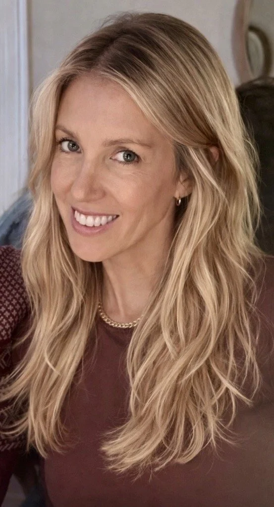 A woman with long blonde hair, smiling, wearing a maroon top, with a gold necklace and hoop earrings.  DC Psychiatry therapy.