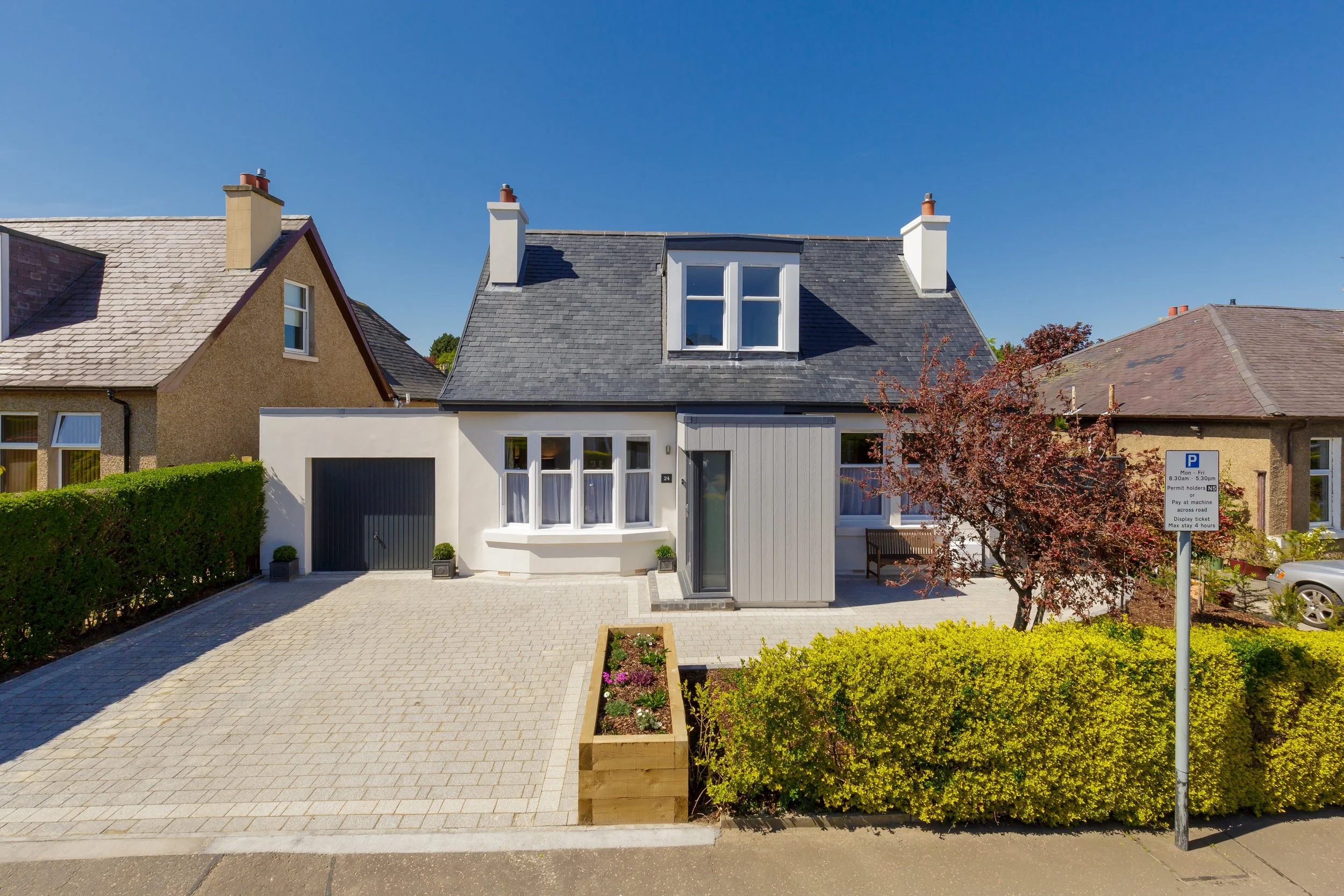 Modern house with gray roof, white exterior, and a small front yard with plants and a paved driveway.
