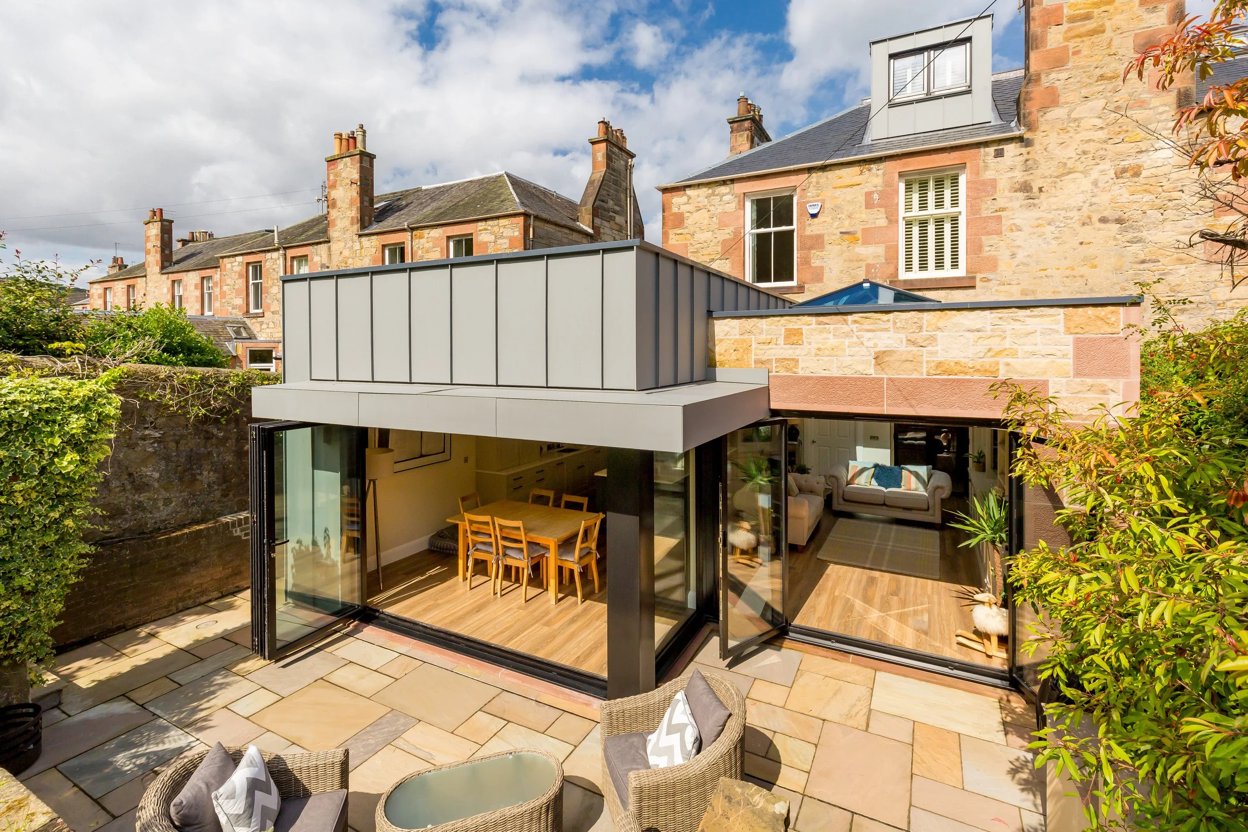 Modern glass extension on a traditional stone house with outdoor patio and garden furniture