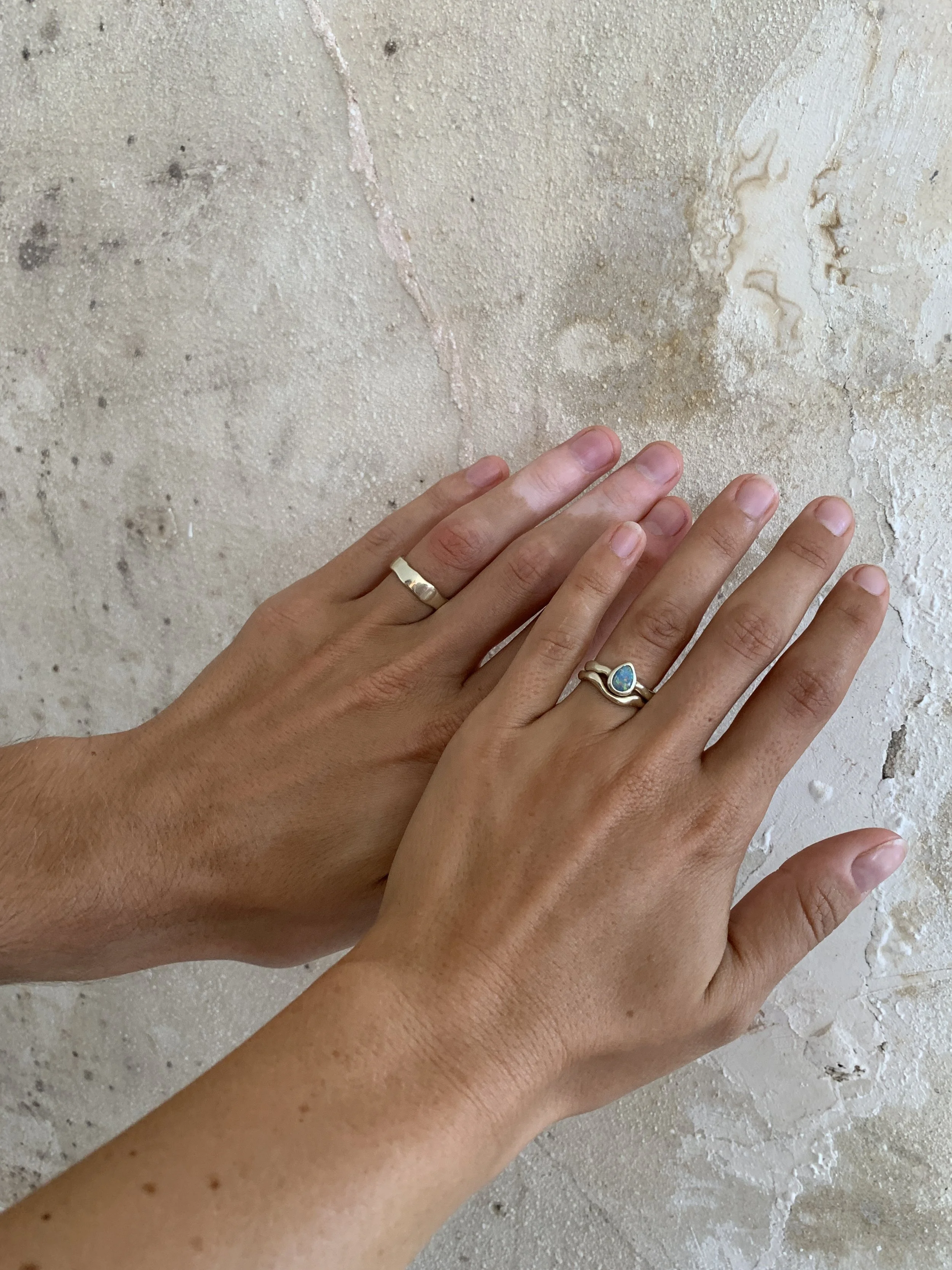 Two hands with rings resting on a textured beige stone surface.
