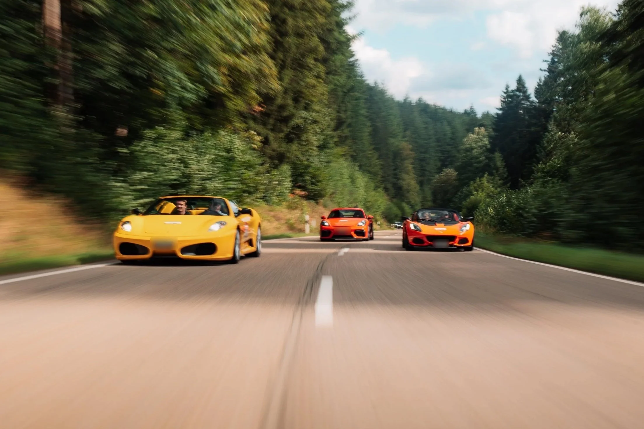 Gelber Ferrari vor zwei orangen Sportwagen auf einer Waldstrasse bei einer früheren One Tank Tour