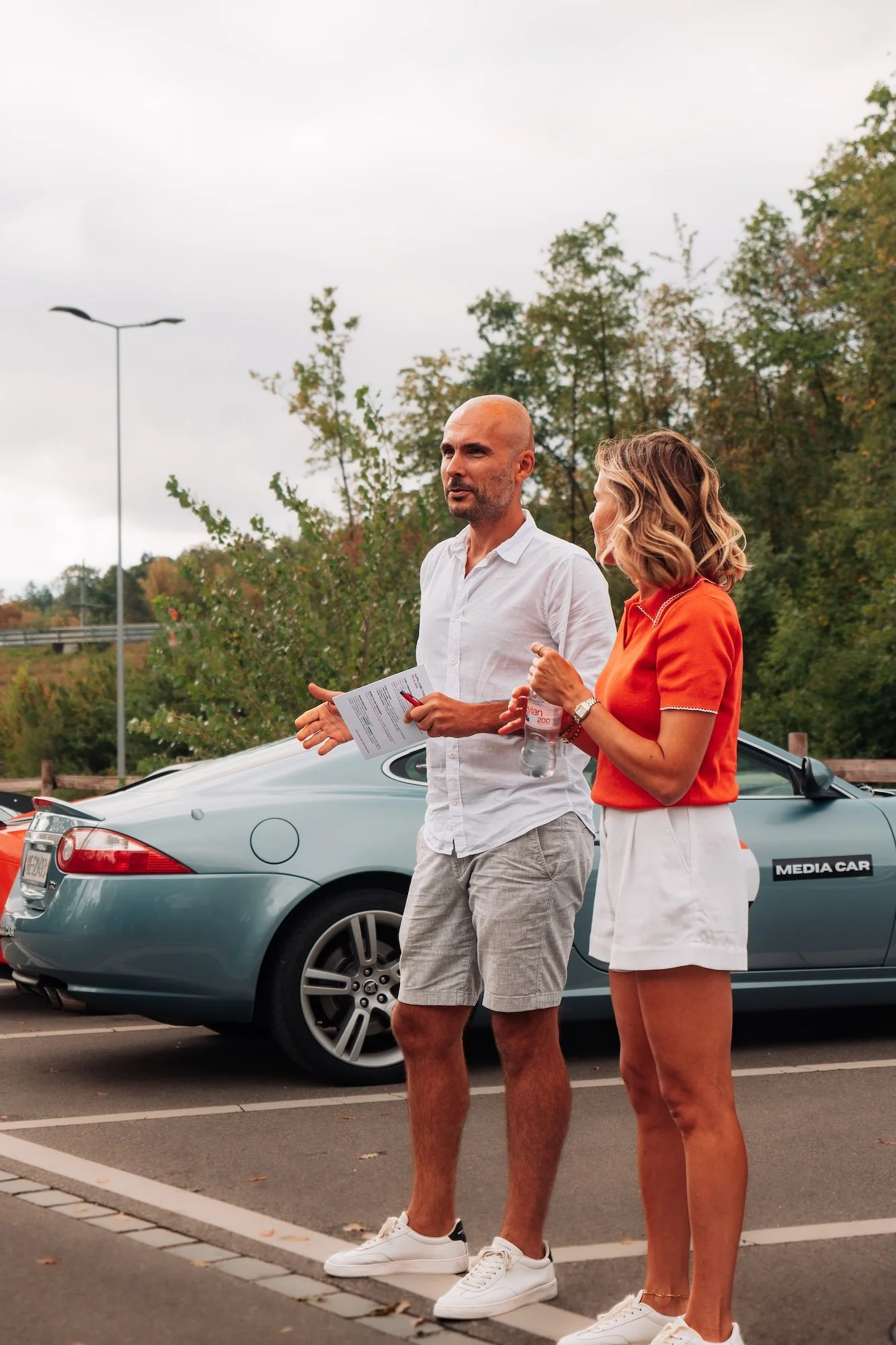 Tour hosts giving the morning briefing beside a silver-blue Jaguar on a previous One Tank Tour