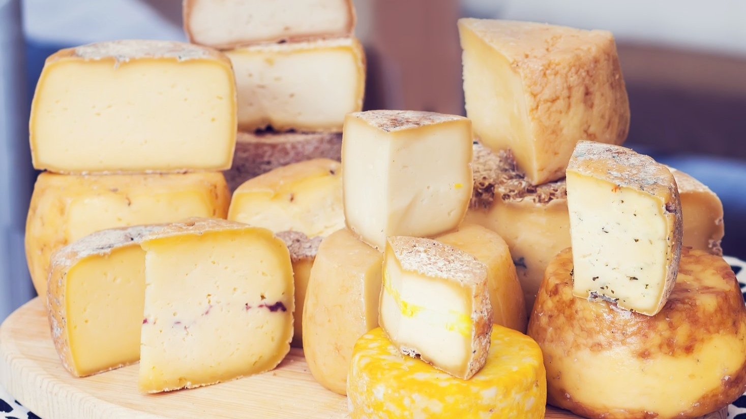 Assorted cheeses of various shapes, sizes, and colors arranged on a wooden surface.