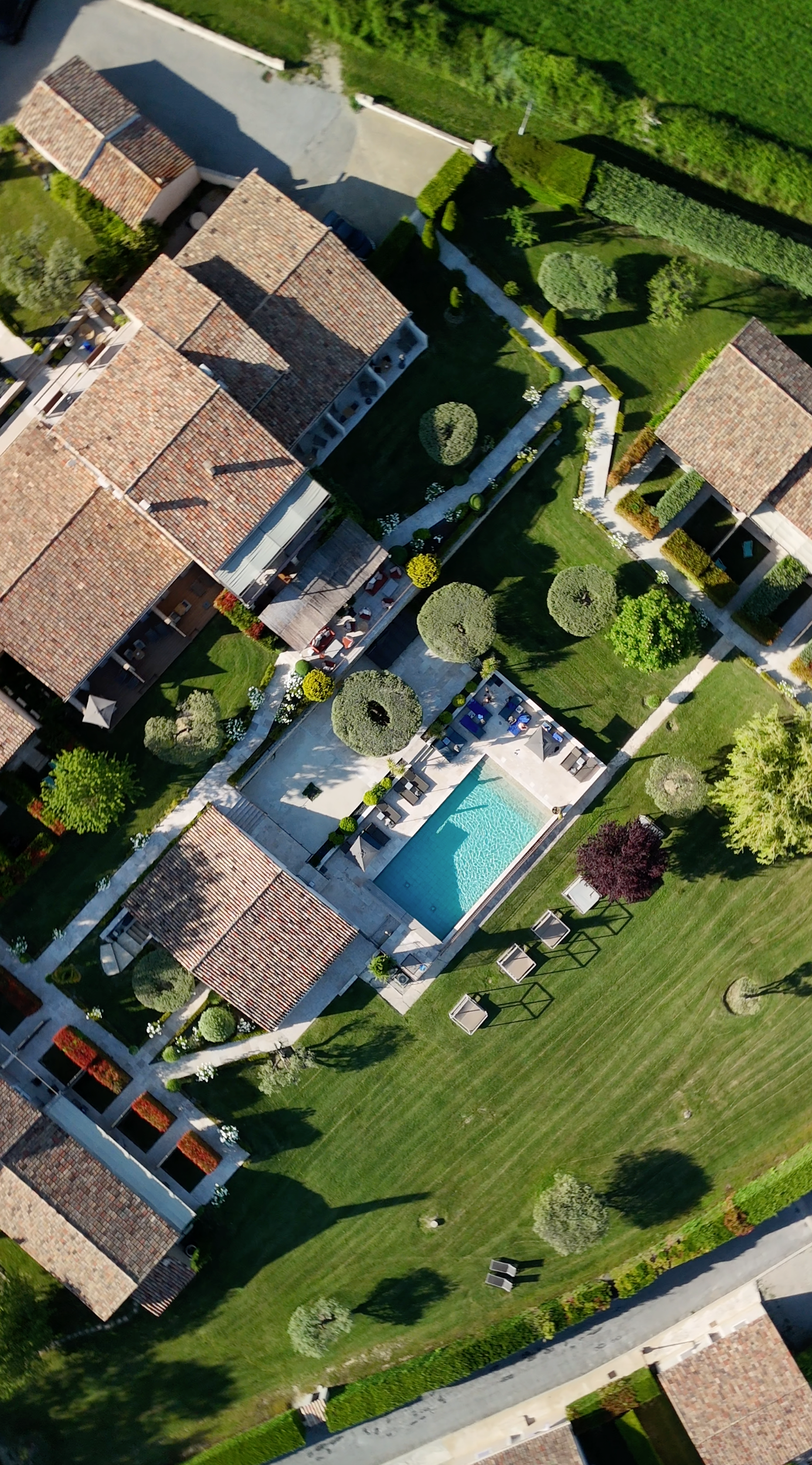 An aerial view of a residential complex with a swimming pool, green lawns, trees, and multiple houses with tiled roofs.
