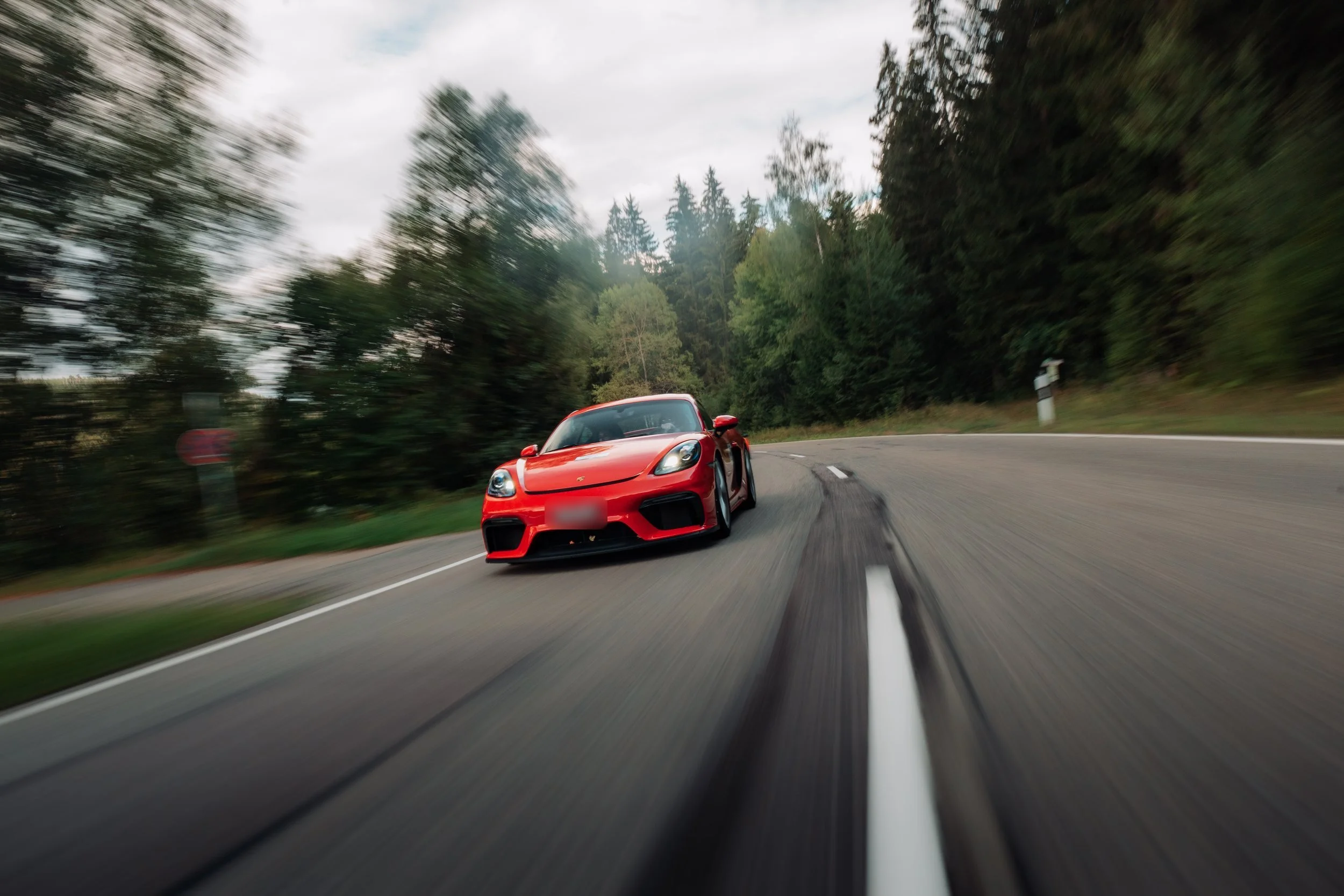 Red Porsche on a forest road, seen from the car ahead, on a previous One Tank Tour