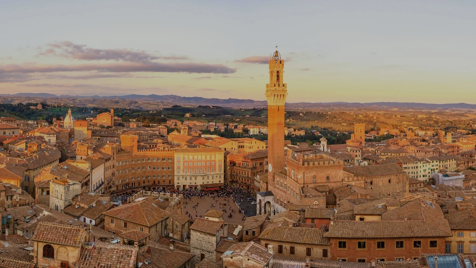 Aerial view of Piazza del Campo in Siena, Italy, with the Torre del Mangia tower and historic Renaissance buildings at sunset.