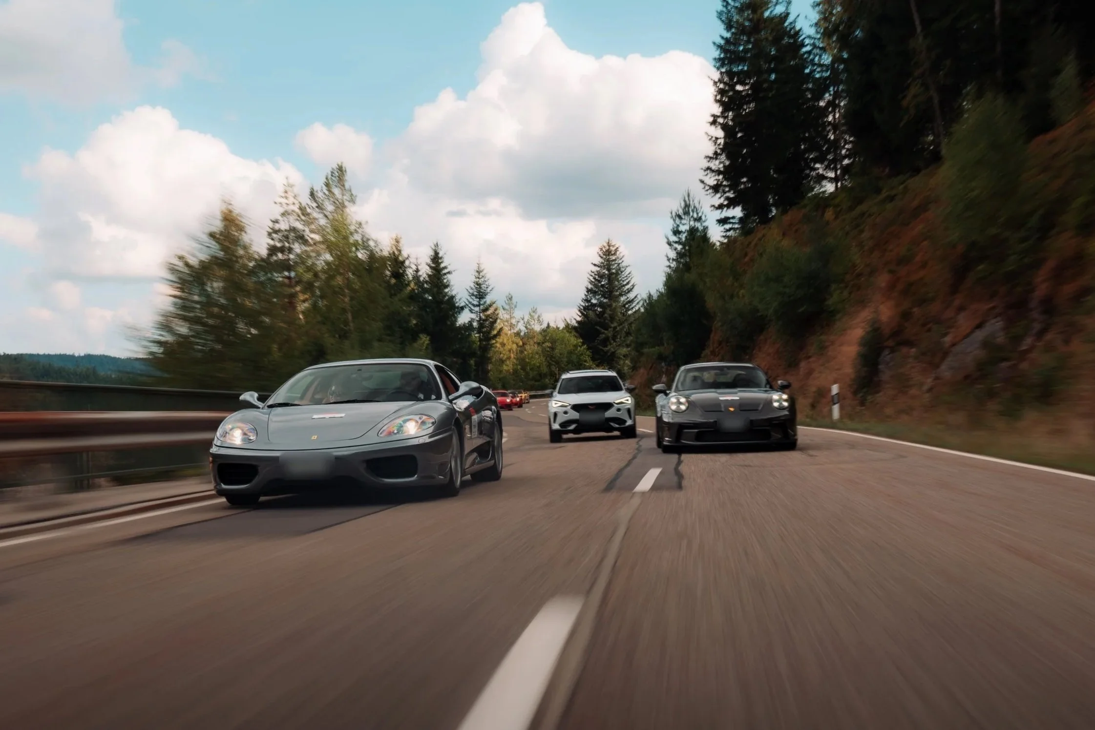 Grauer Ferrari 360 vor zwei Autos auf offener Strasse unter weitem Himmel bei einer früheren One Tank Tour