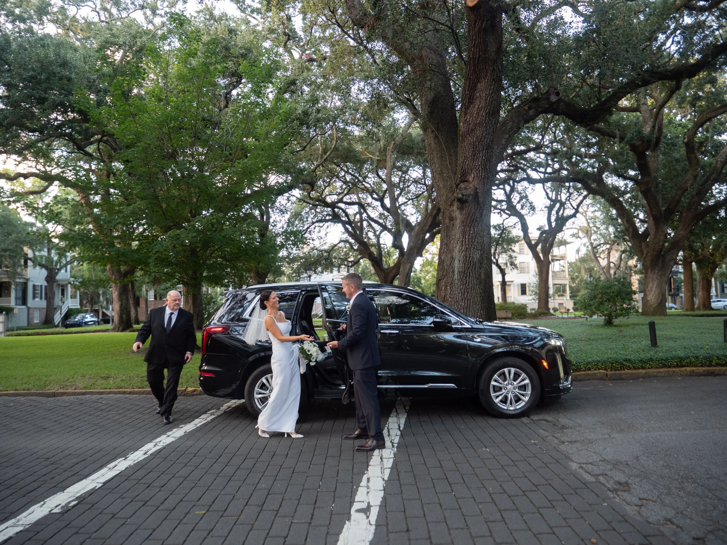 Bride and groom returning to their waiting black SUV beside a Savannah square