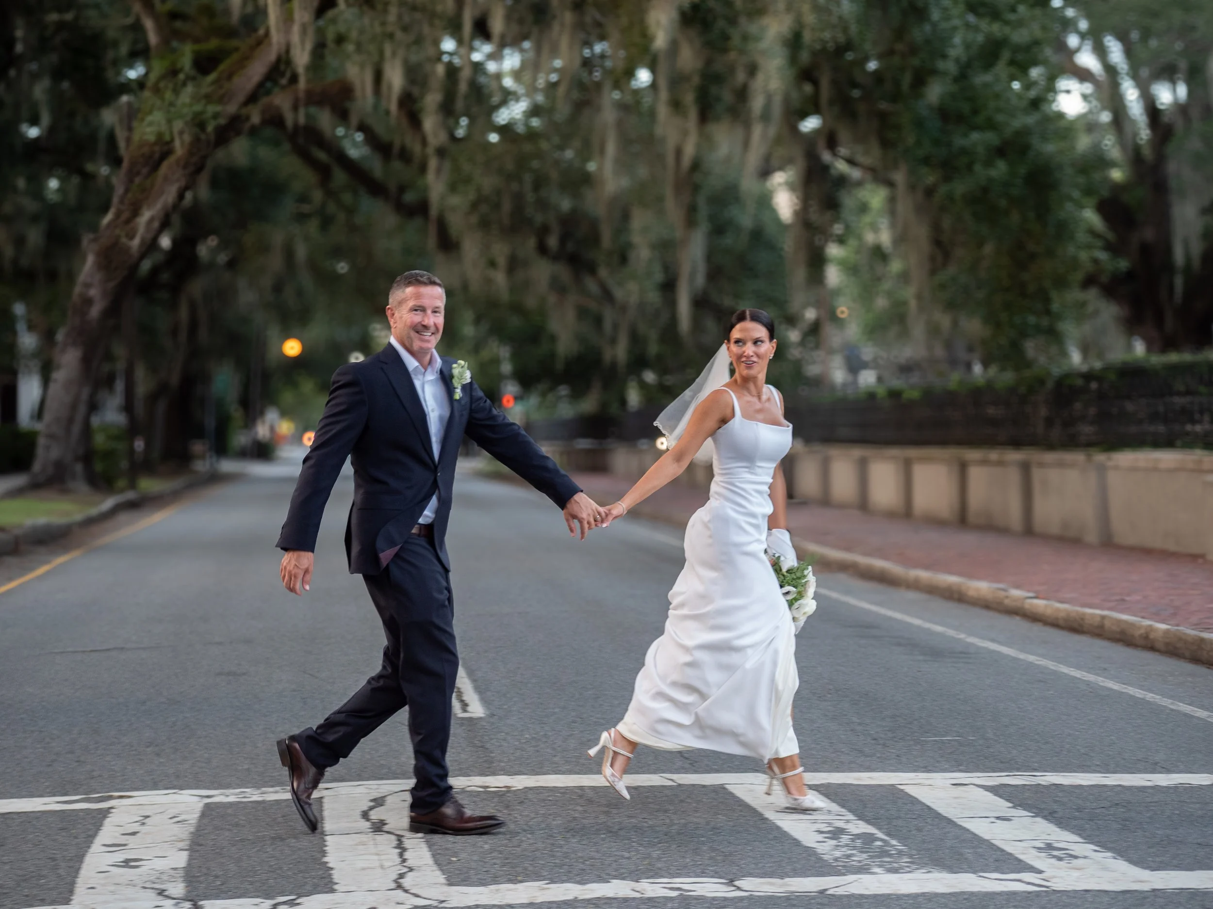 Bride and groom smiling and holding hands while crossing a street in Savannah