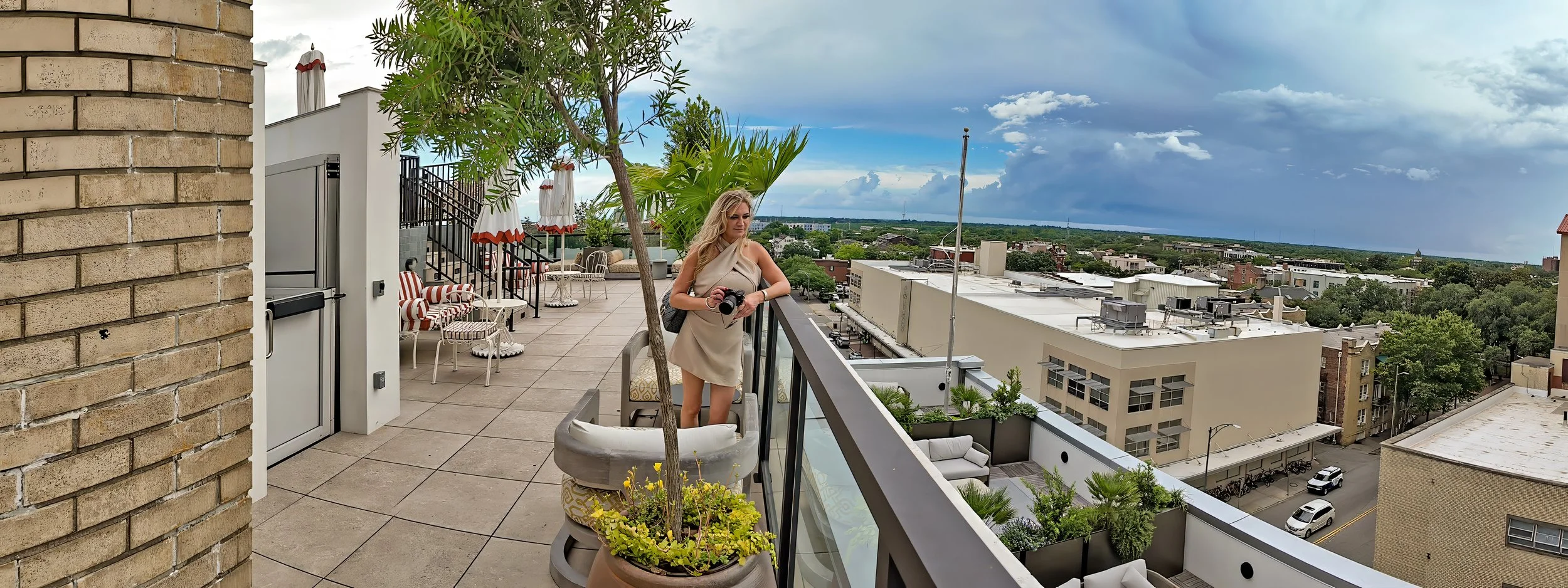 Woman holding a camera in the rooftop lounge at The Sun Club at Municipal Grand with Savannah skyline views in the background