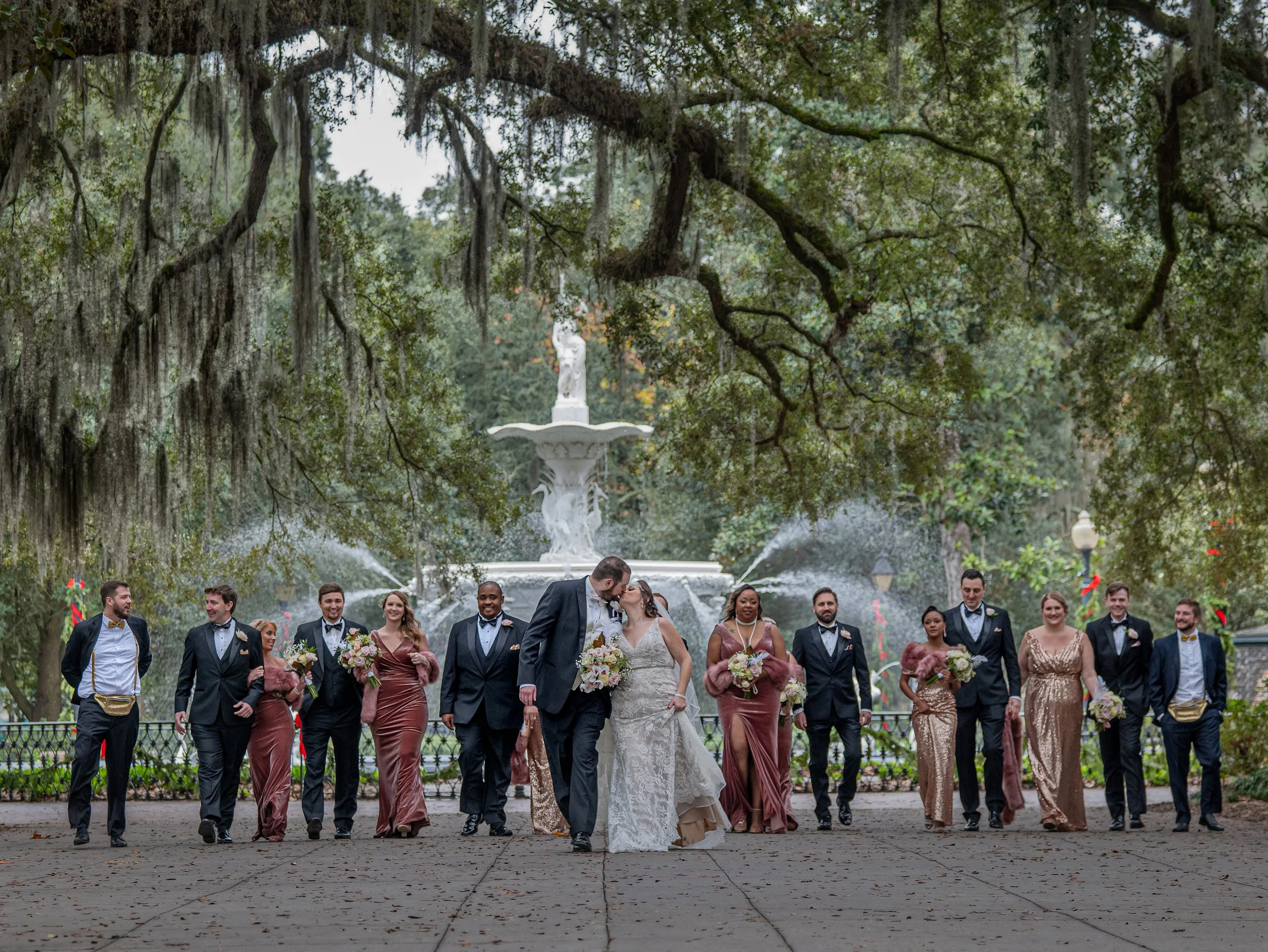 Wedding party walks down the Forsyth Park promenade with the iconic Savannah fountain in the background during a luxury Savannah wedding celebration.