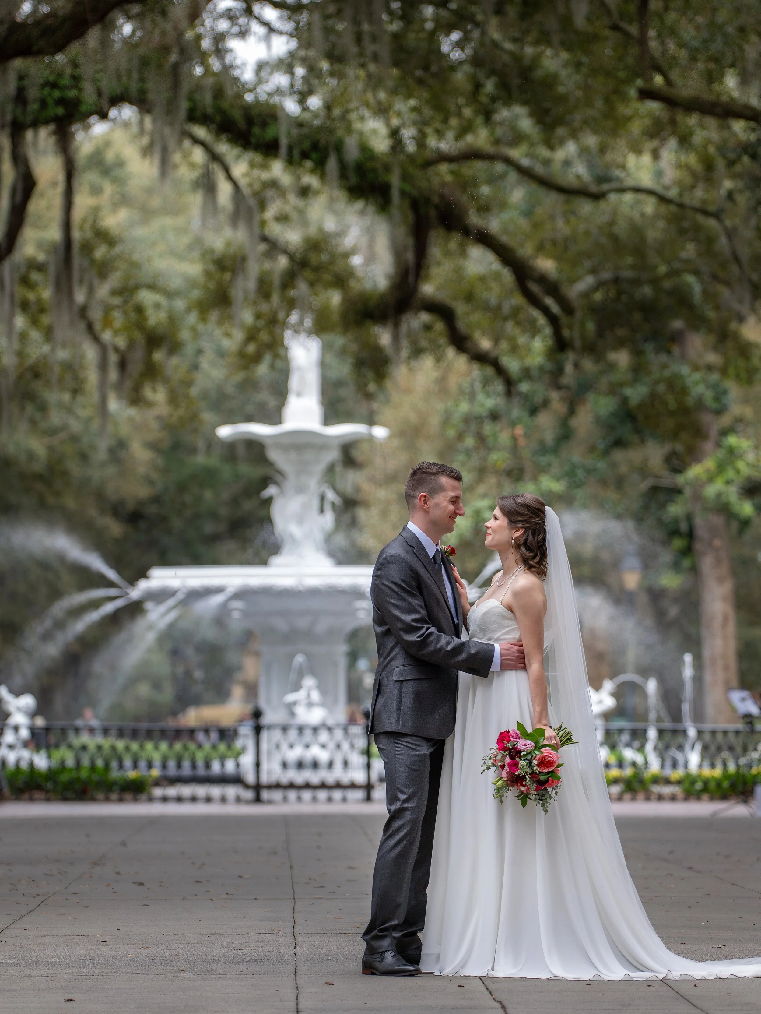 Tim and Daniella pause for a portrait along the Forsyth Park promenade with the fountain visible in the distance after their Savannah wedding ceremony.