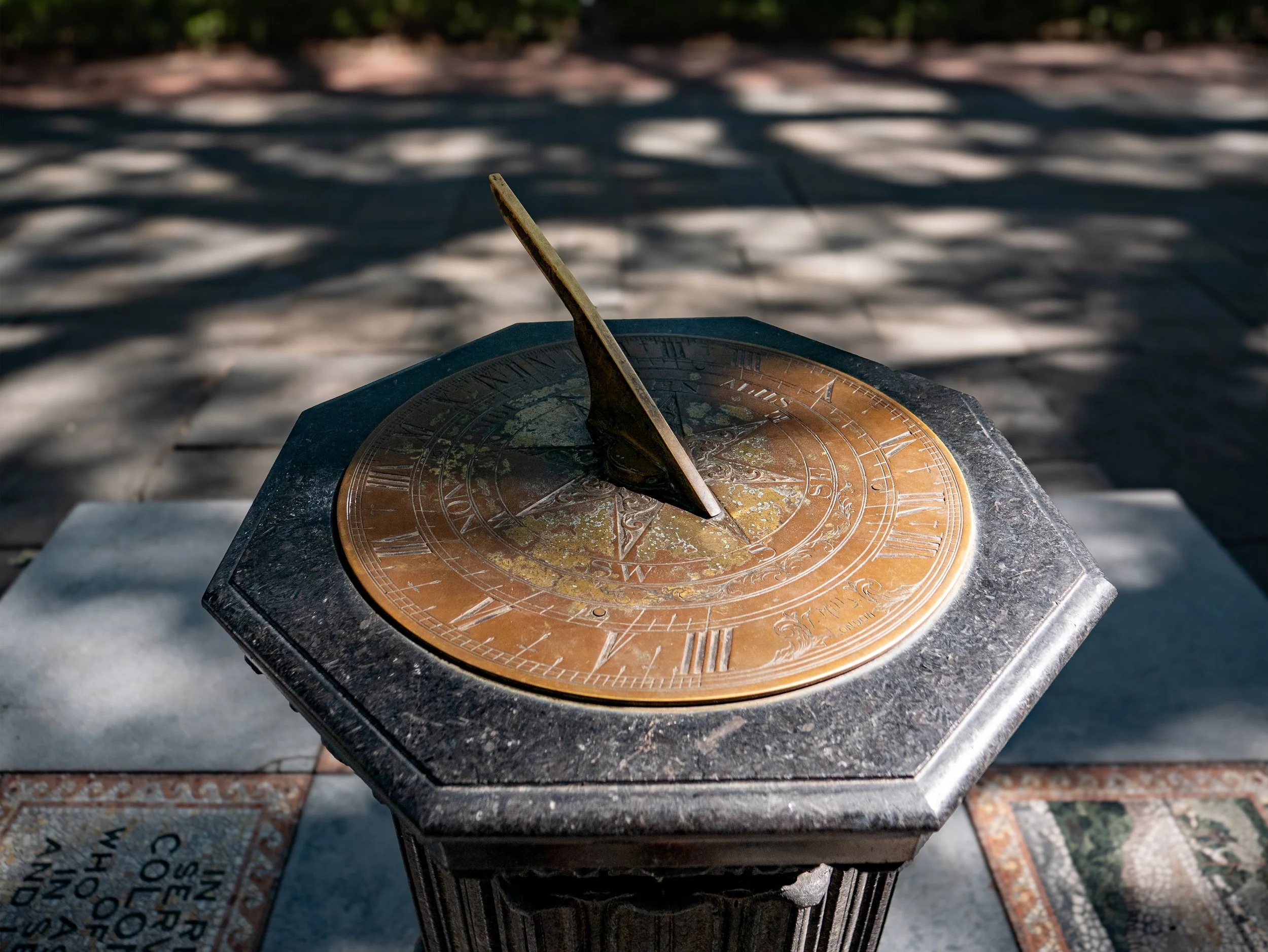Close view of the bronze sundial in Johnson Square with sunlight and tree shadows.