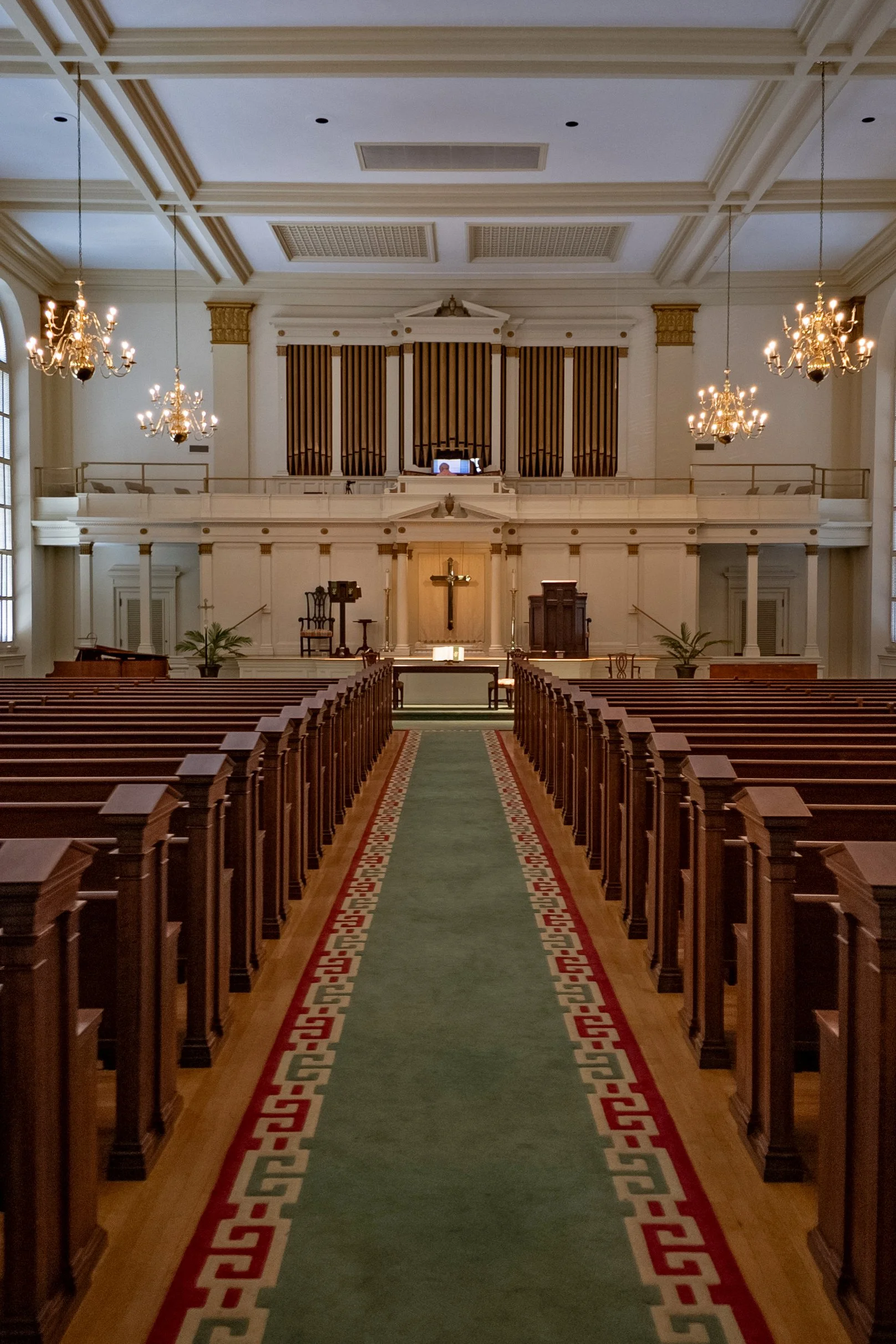 First Baptist Church sanctuary with wooden pews, a central aisle, chandeliers, and organ pipes above the front.