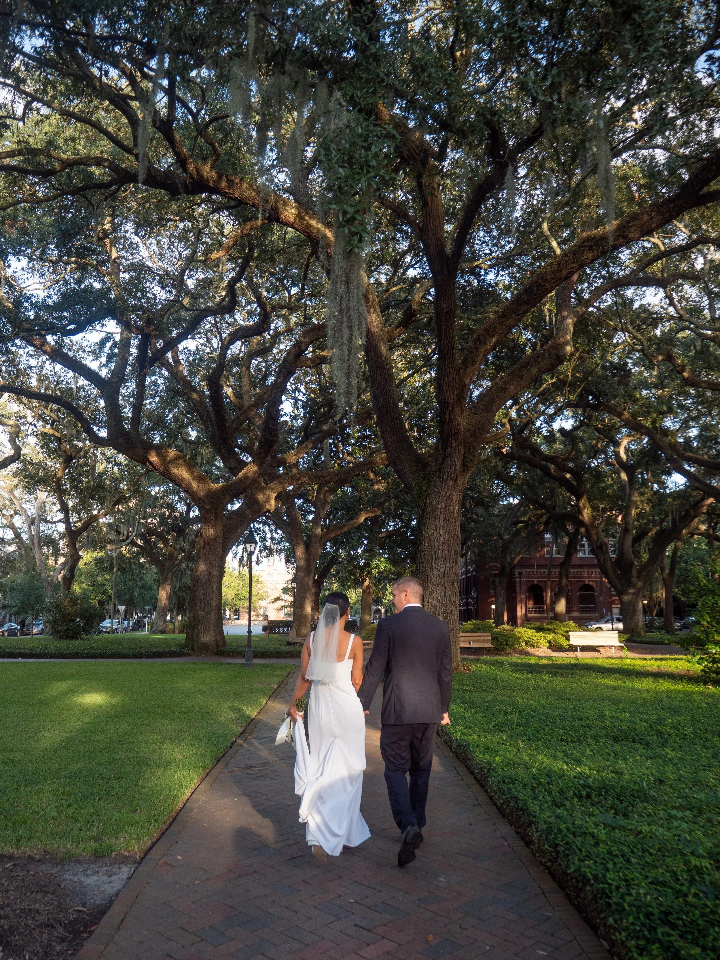 Bride and groom walking beneath the live oaks in Pulaski Square before their ceremony