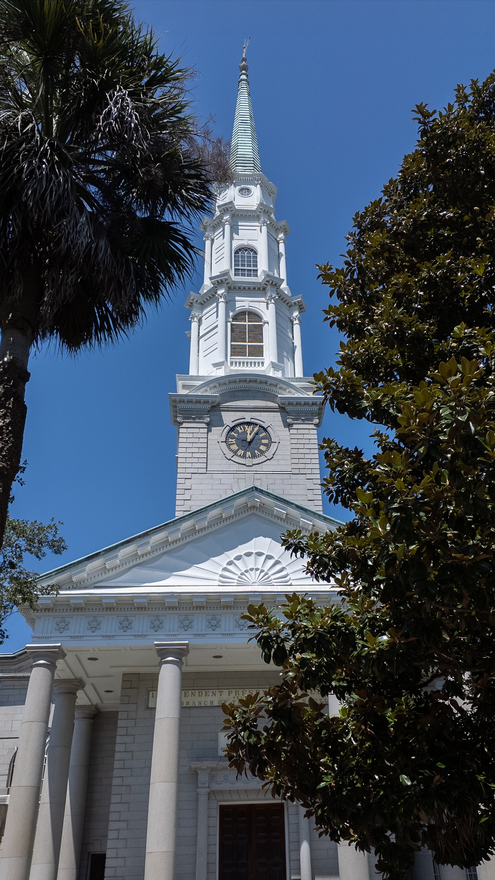 Independent Presbyterian Church’s white steeple and clock tower framed by trees on Bull Street in Savannah.