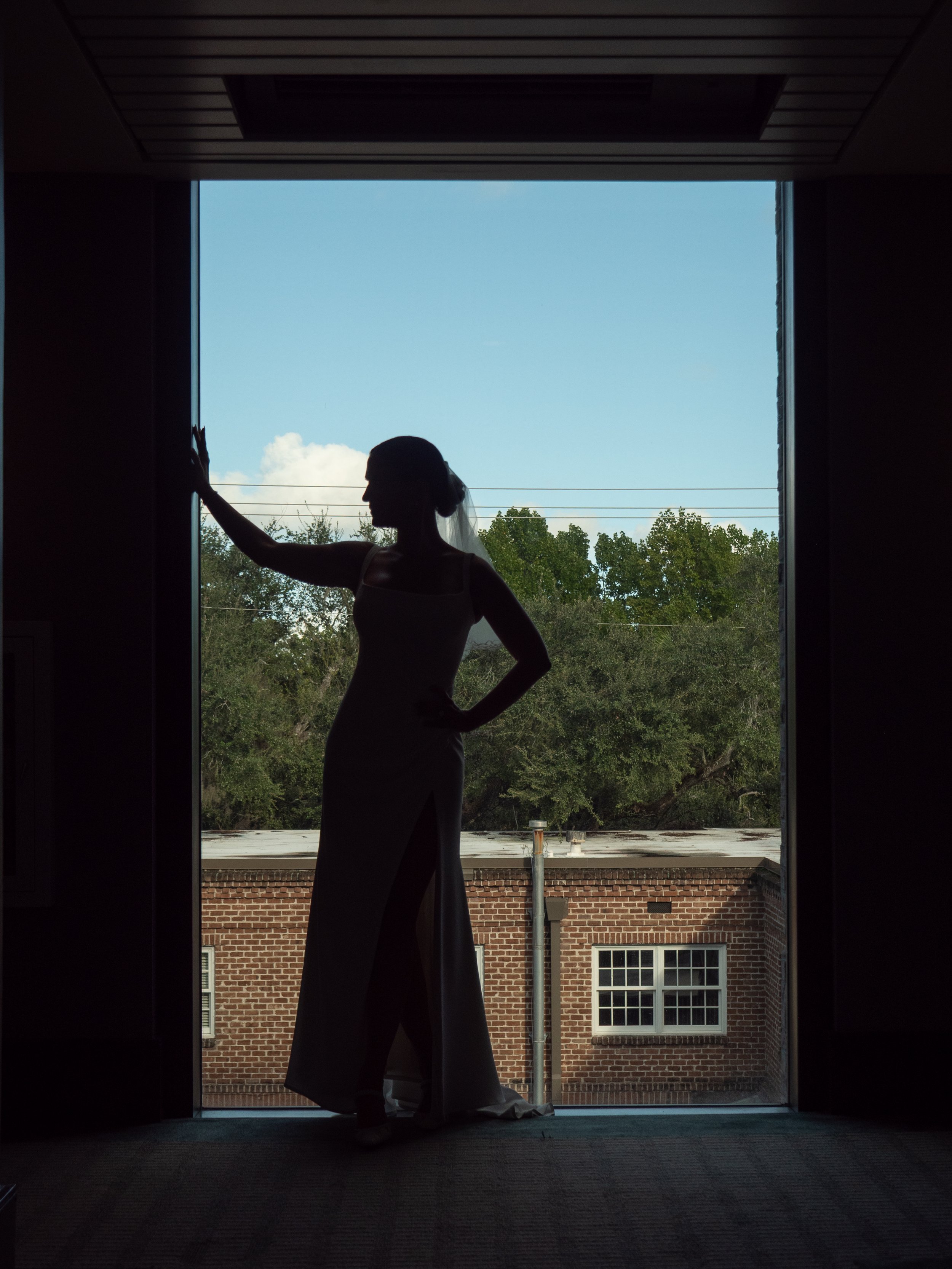 Silhouette of the bride in her wedding dress standing before a window overlooking Savannah