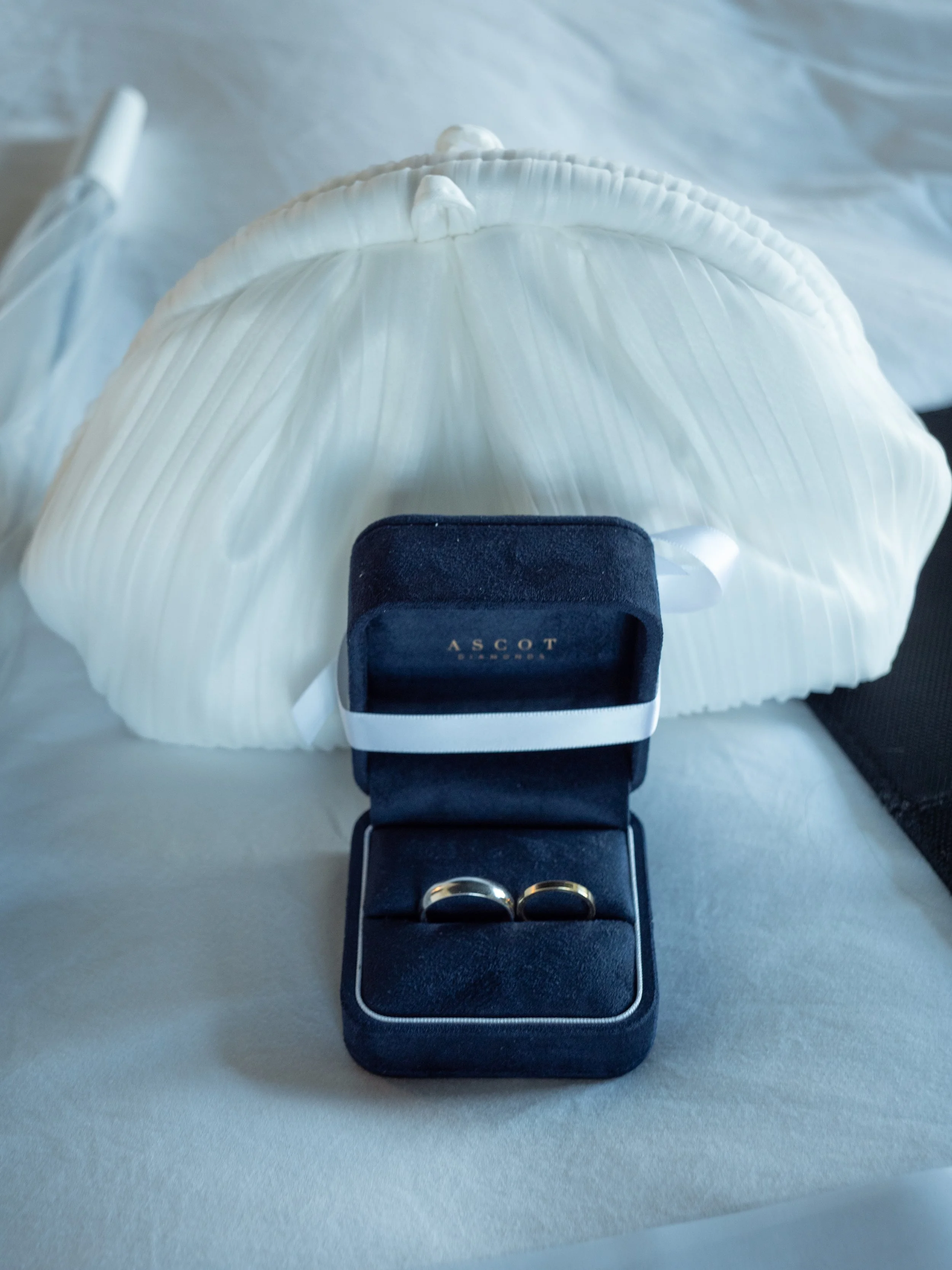 Wedding rings in a blue ring box displayed with the bride’s white wedding dress