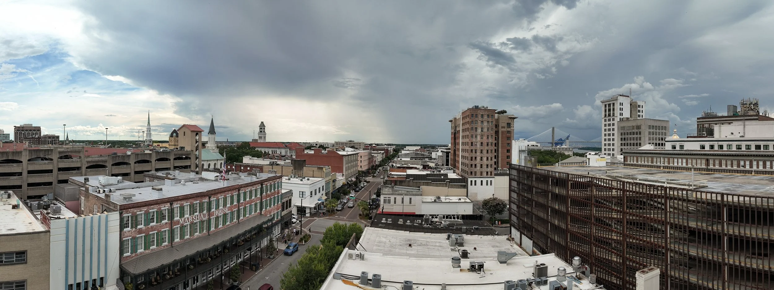Panoramic view of Savannah skyline from The Sun Club rooftop at Municipal Grand featuring historic church steeples and the Talmadge Bridge