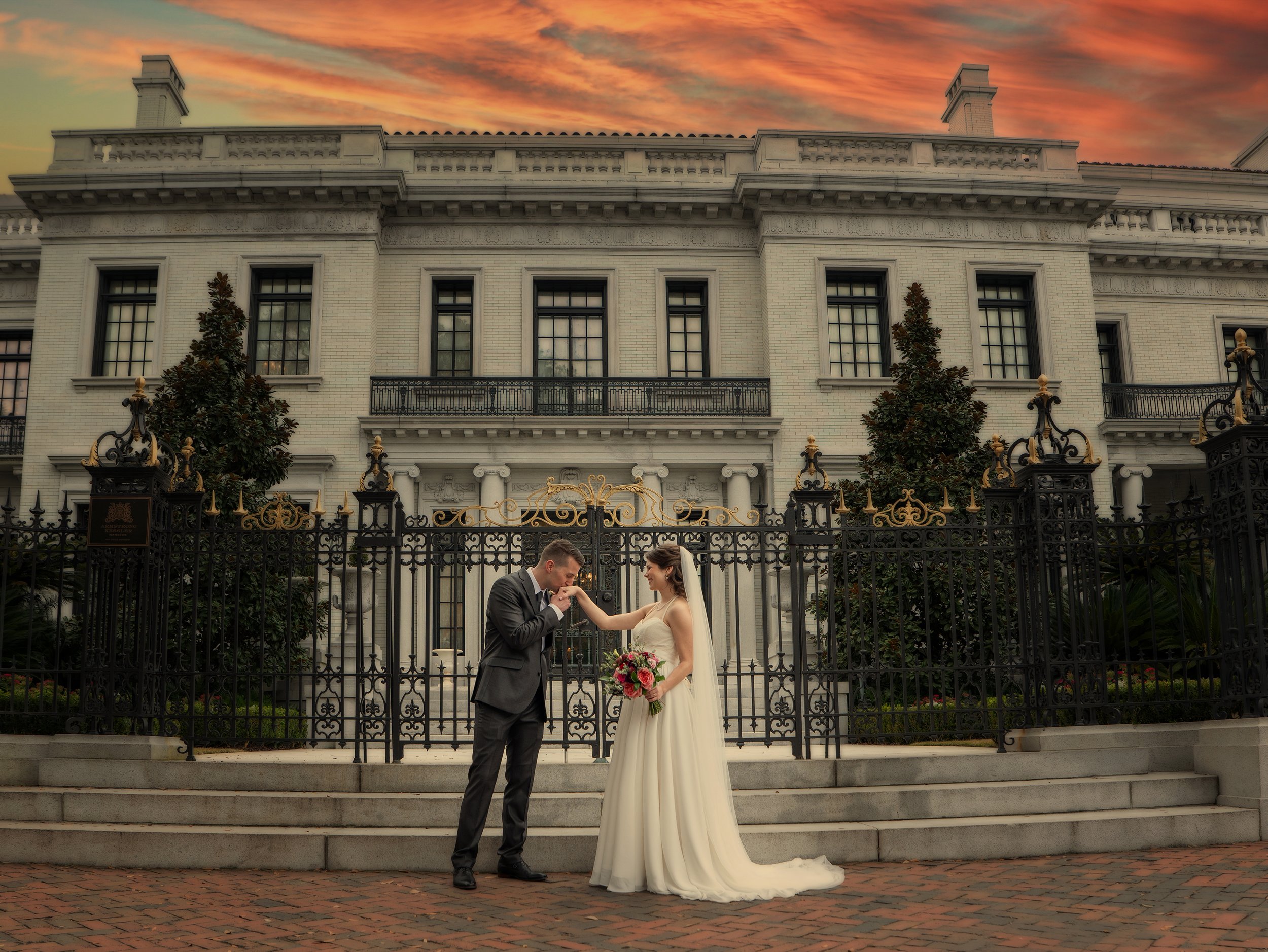 Groom kisses the bride’s hand in front of the historic Armstrong Kessler Mansion during a luxury Savannah wedding celebration in downtown Savannah, Georgia.