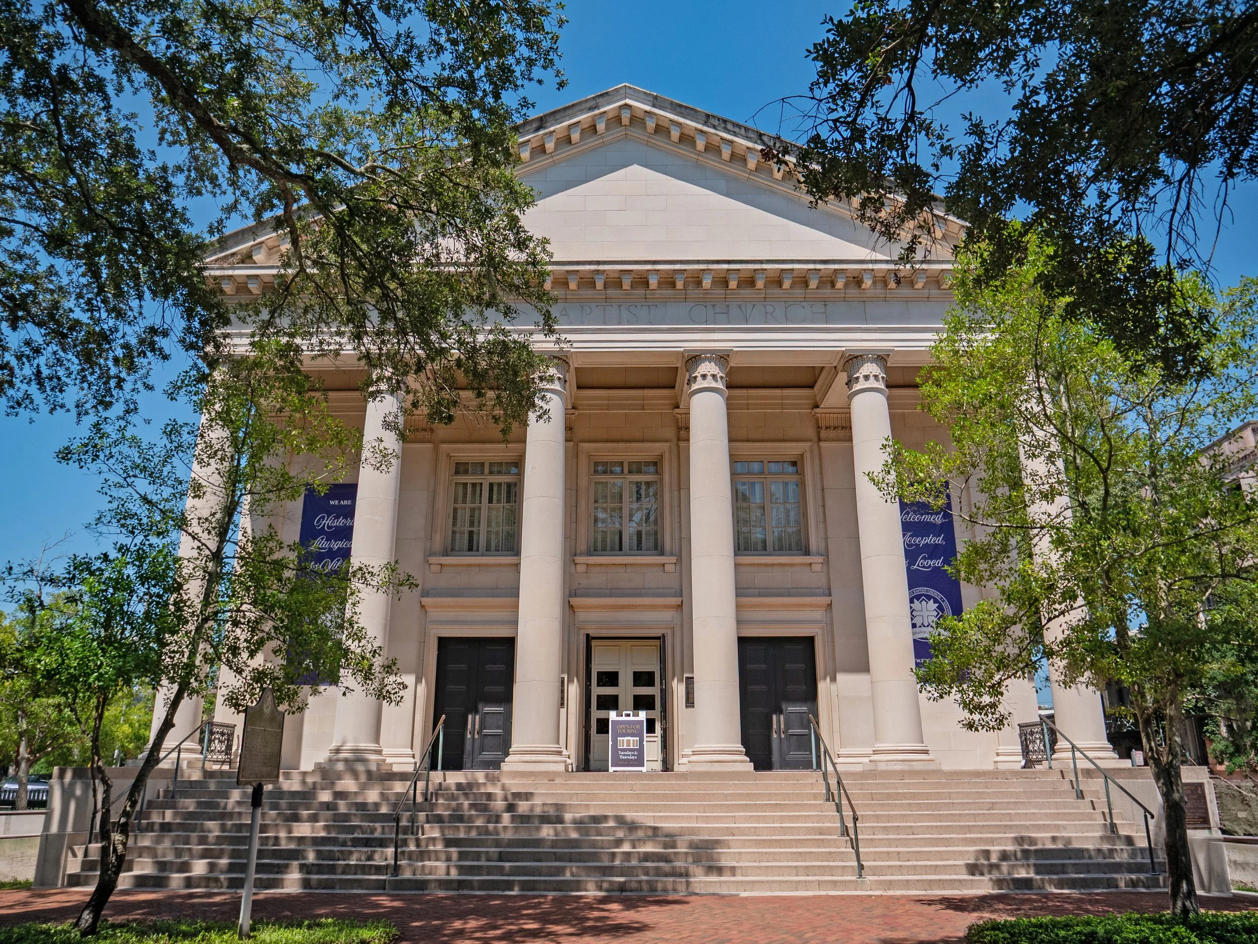 Columned front facade of First Baptist Church in Savannah framed by leafy branches.