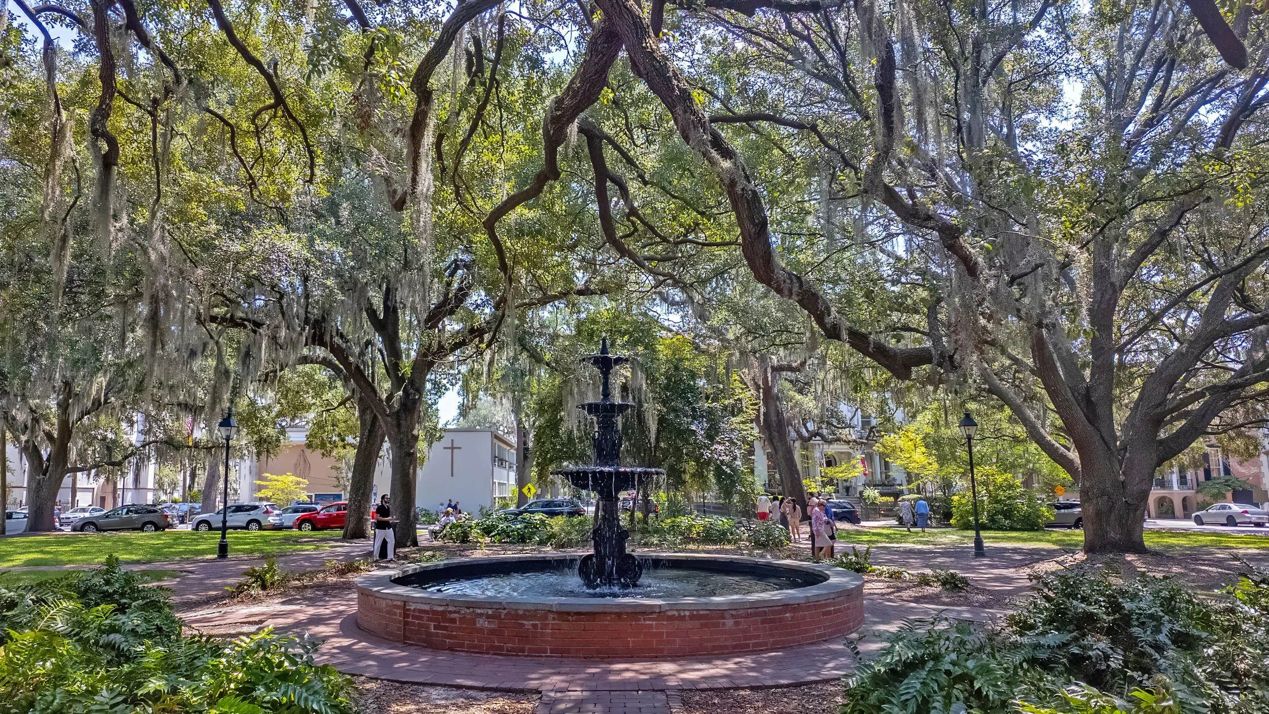 Wide-angle view of the three-tiered fountain in Lafayette Square surrounded by trees and historic Savannah architecture.