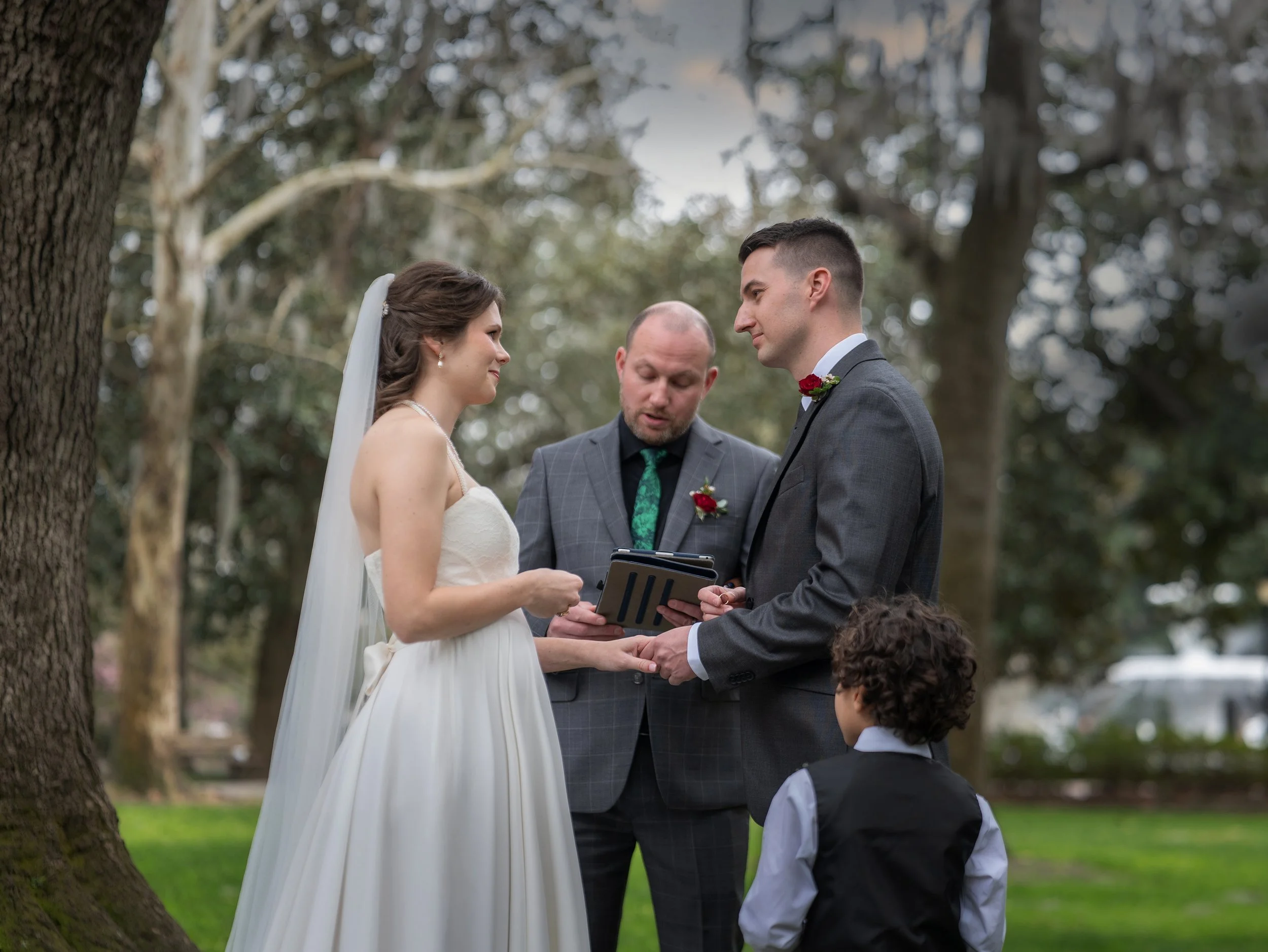 Tim and Daniella exchange rings as their child looks up at them during their intimate Forsyth Park wedding ceremony.