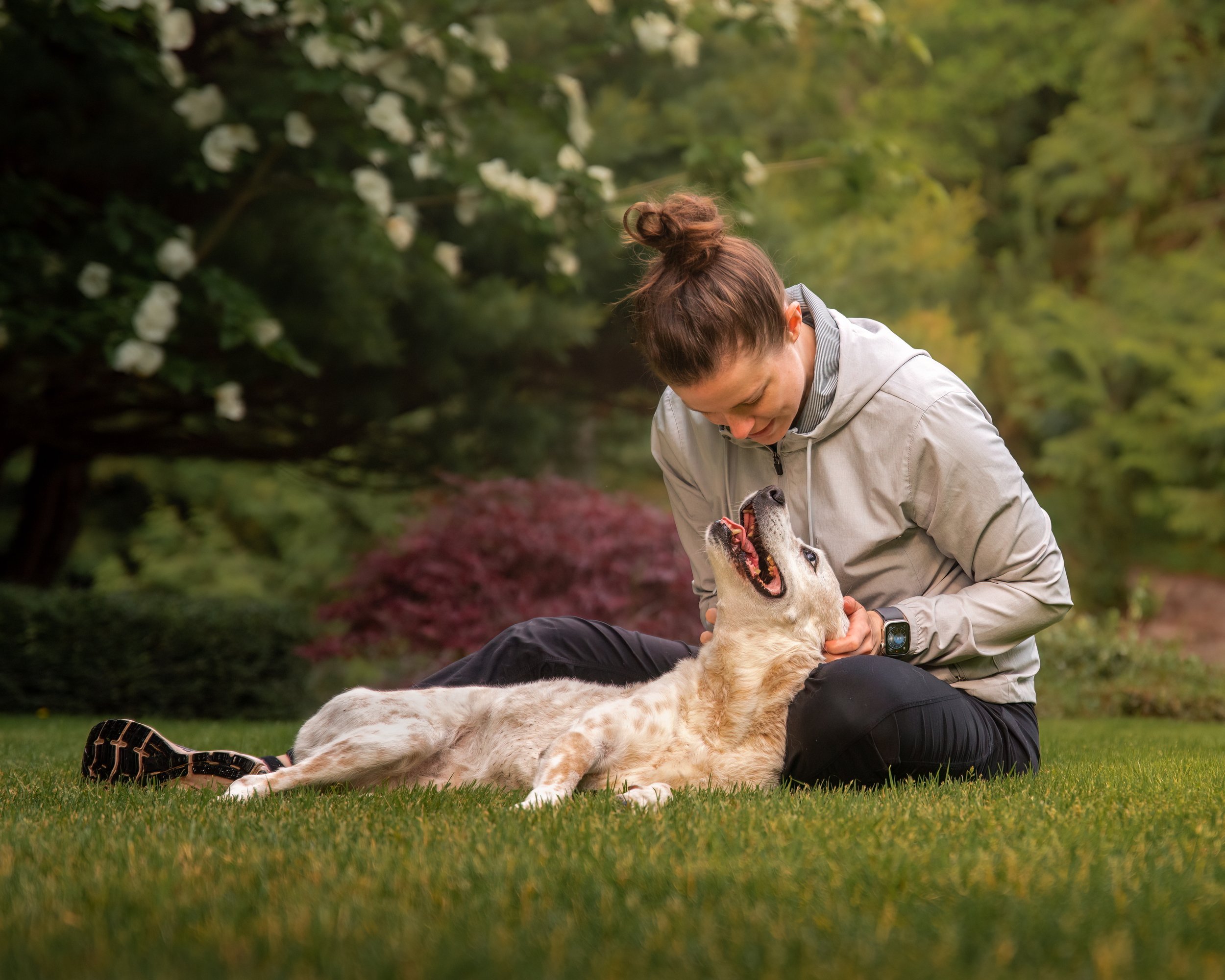 portrait of a dog mom sitting in the grass with her dog laying in her lap, both looking at each other in Puyallup