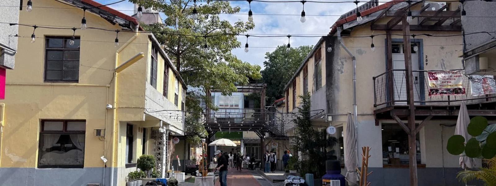 image	String lights over a courtyard between yellow historic dorm buildings at Shengji New Village in Taichung