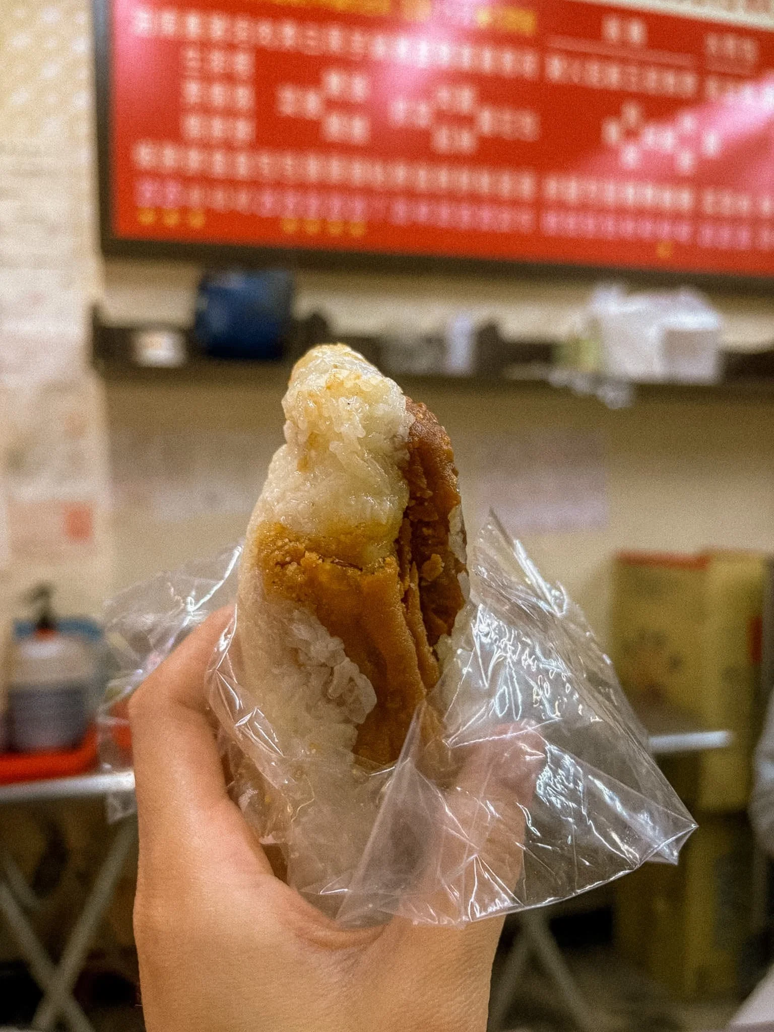 Sticky rice roll (fan tuan) with a savory filling, wrapped in plastic at a Taiwanese breakfast shop