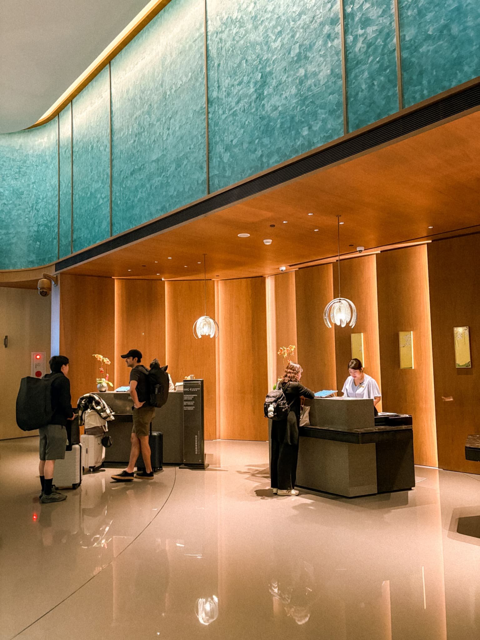 Guests checking in at InterContinental Kaohsiung front desk with warm wood interiors and teal accent wall