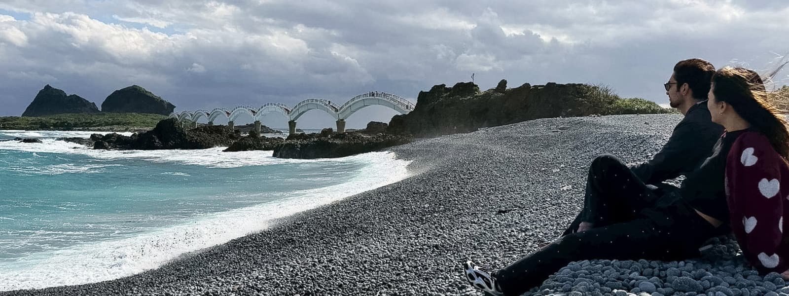Melinda and Gabe sitting on Sanxiantai's pebble beach admiring the eight-arch bridge, Taitung, Taiwan