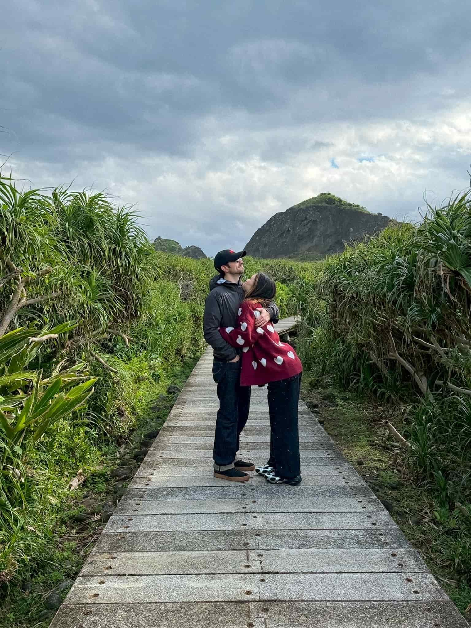 Gabe Melinda embracing on the Sanxiantai trail boardwalk surrounded by coastal greenery, Taitung