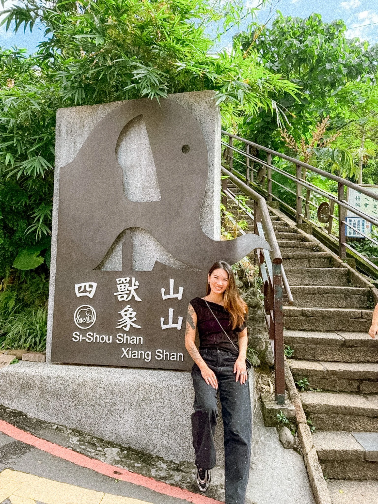 Elephant Mountain trail entrance in Taipei with Melinda sitting in front of the sign before starting the hike