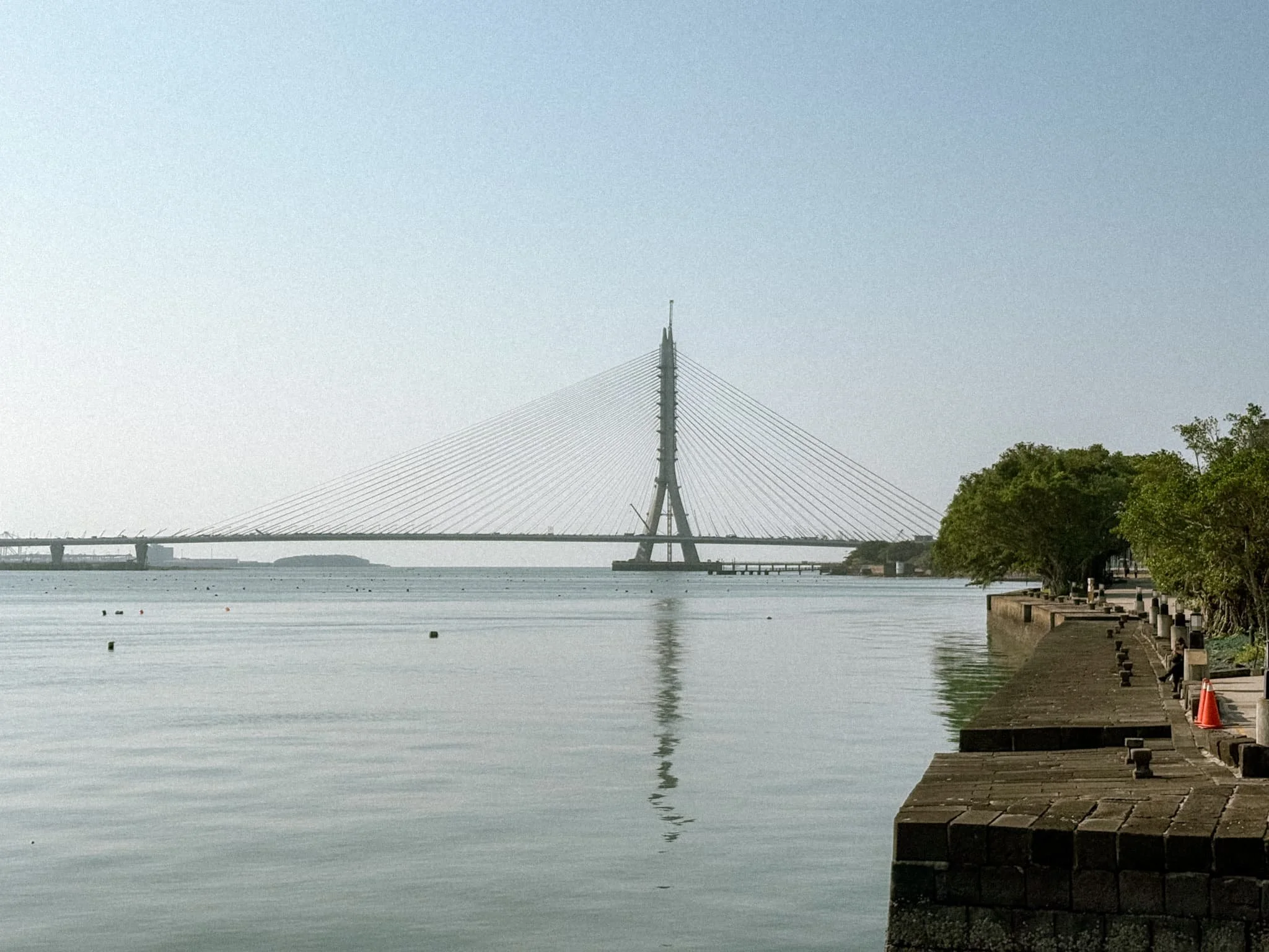 Zaha Hadid-designed cable-stayed bridge reflected in the Tamsui River, seen from the waterfront promenade
