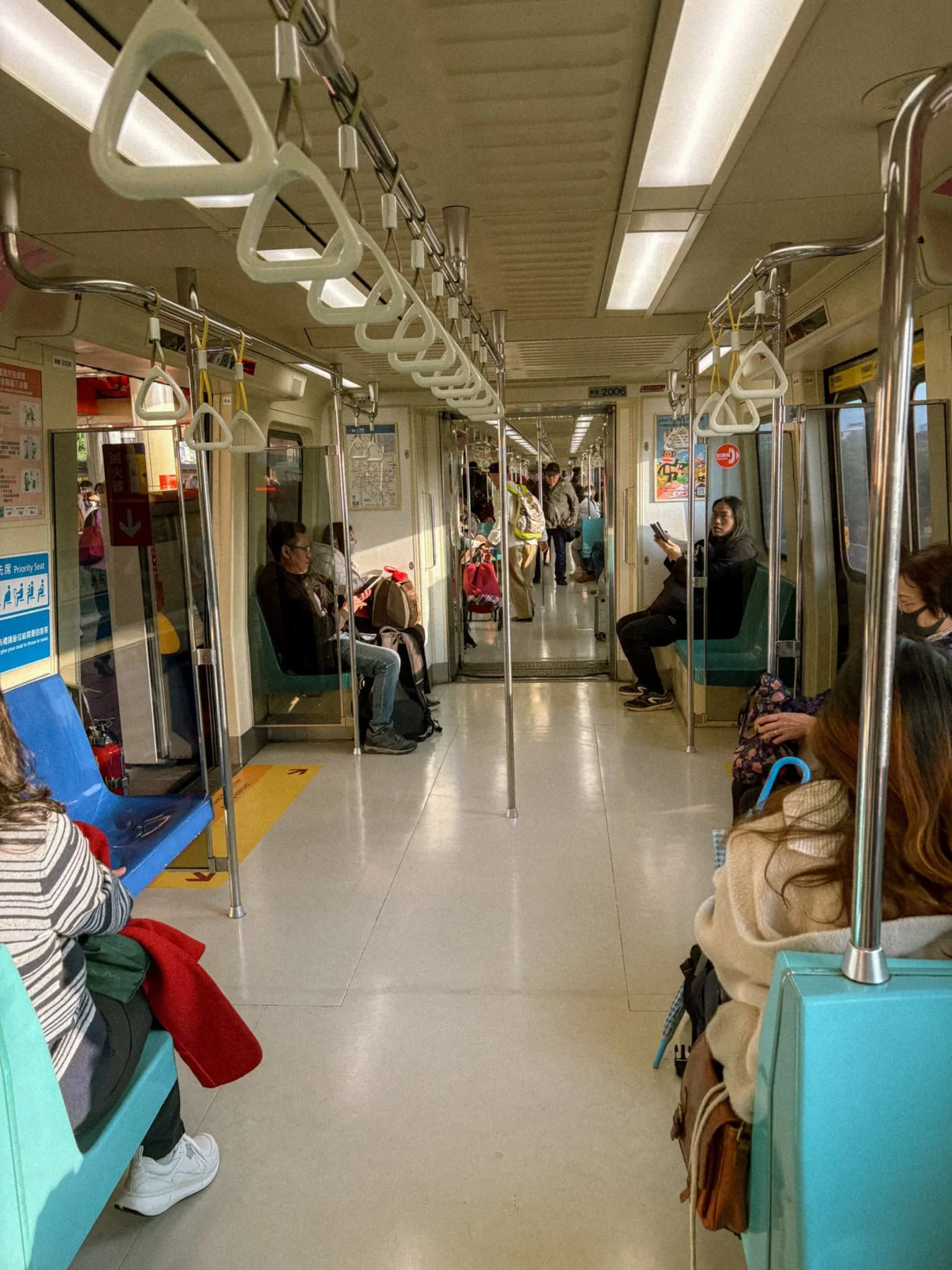 Inside a Taipei MRT red line train with teal seats, white hand straps, and passengers on the way to Tamsui