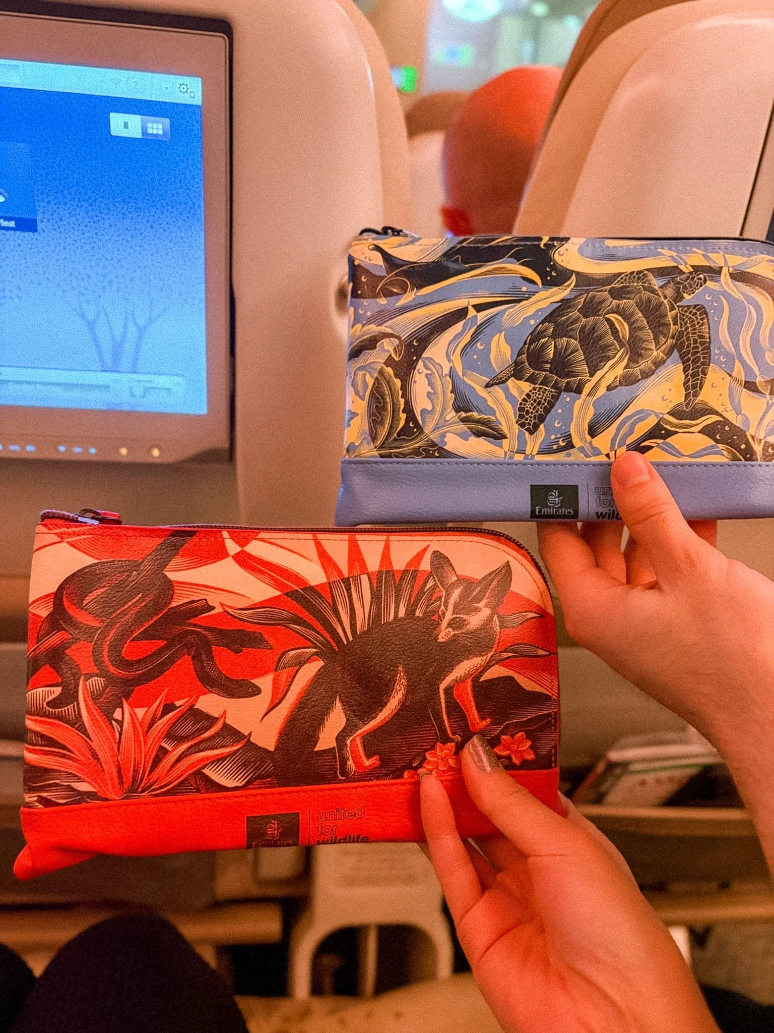 Emirates Premium Economy amenity kit with floral design showing two pouches held up on the A380 cabin