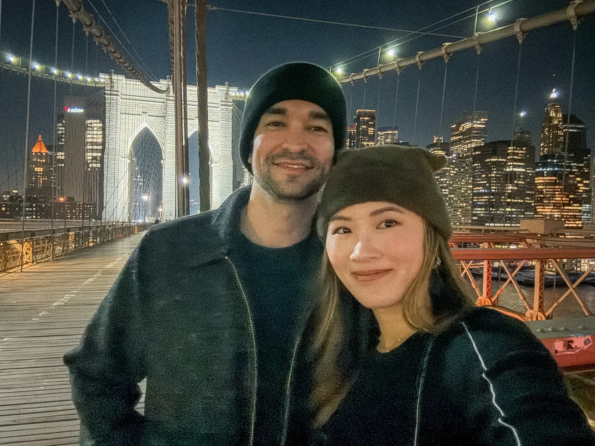 Couple walking across the Brooklyn Bridge at night with Manhattan skyline lit up in the background