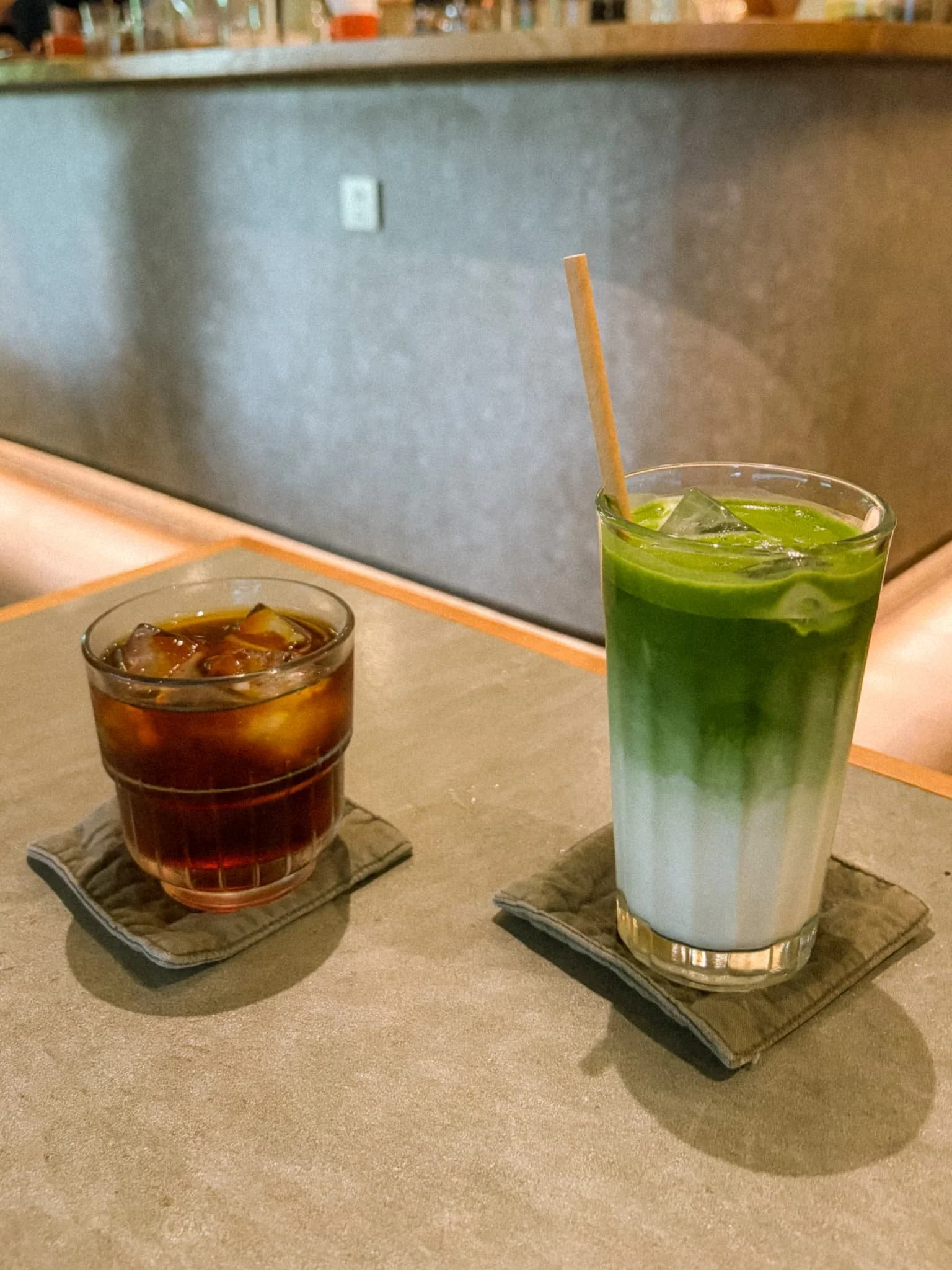 Layered iced matcha latte and iced coffee on a concrete table at a minimalist upstairs cafe in Saigon, Vietnam