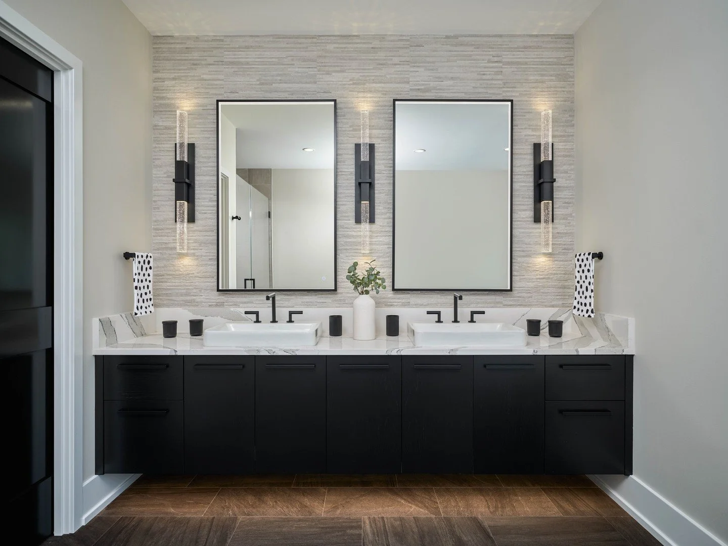 This primary bathroom came a long way from exposed studs and plumbing, becoming a space defined by simplicity, contrast, and bold details. Dark cabinetry from @kountrykraftcabinetry and black fixtures add definition, while warm tile, light countertop