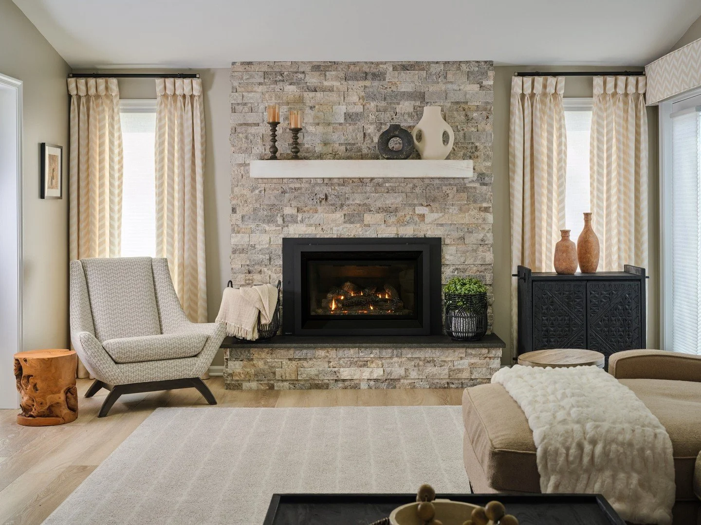 For Thornbury, the fireplace became the starting point for the transformation. We replaced the original brick with a lighter stone surround and simplified the mantel, then carried that softer direction throughout the room with warm neutrals, natural 