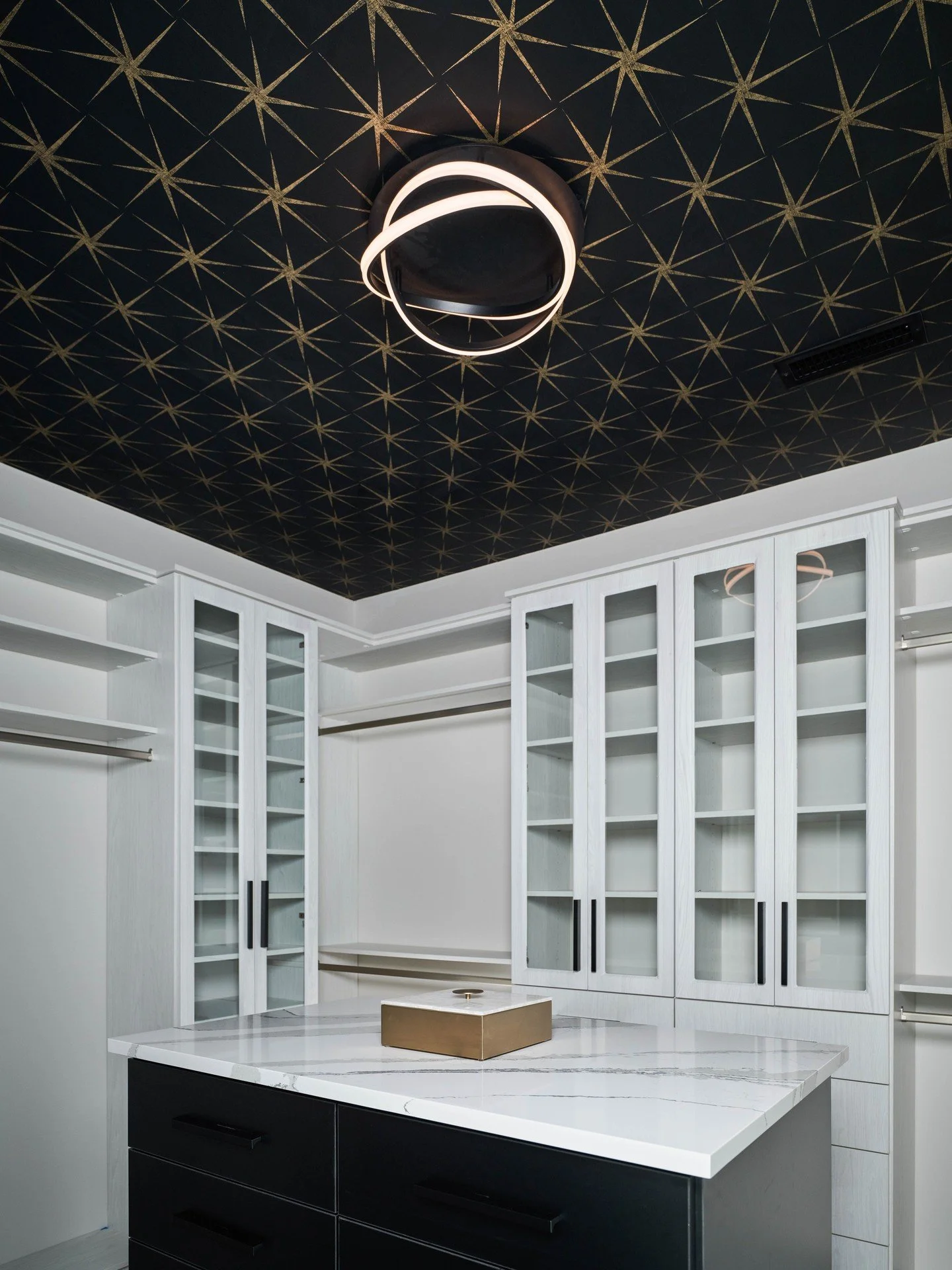 A closet with a dress code: black, white, and a  touch of gold. ✨⁠
⁠The Sandra Court primary closet balances clean custom cabinetry with a bold @york_wallcoverings ceiling and sculptural lighting. Functional below, fun overhead.⁠
⁠
📸: @giannelliphot