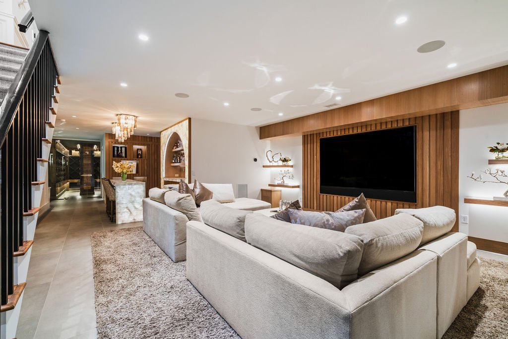 Home theatre with two couches, a large tv and a walkway leading to a bar and wine cellar.