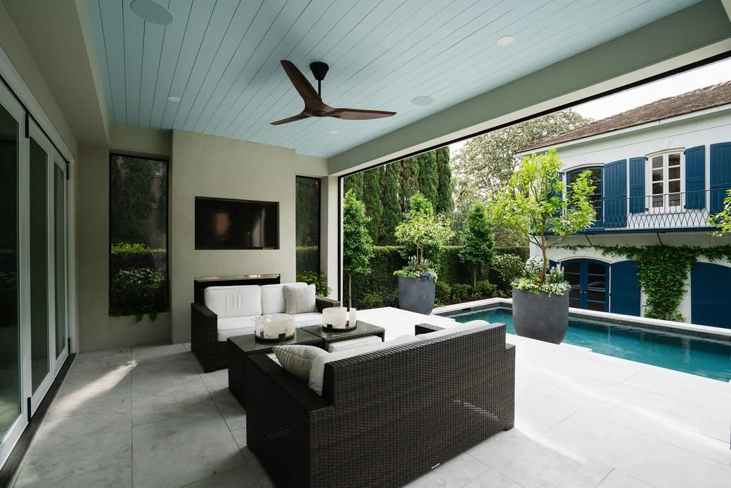 Covered outdoor living area with wicker seating, fireplace, ceiling fan and views of a private courtyard pool.