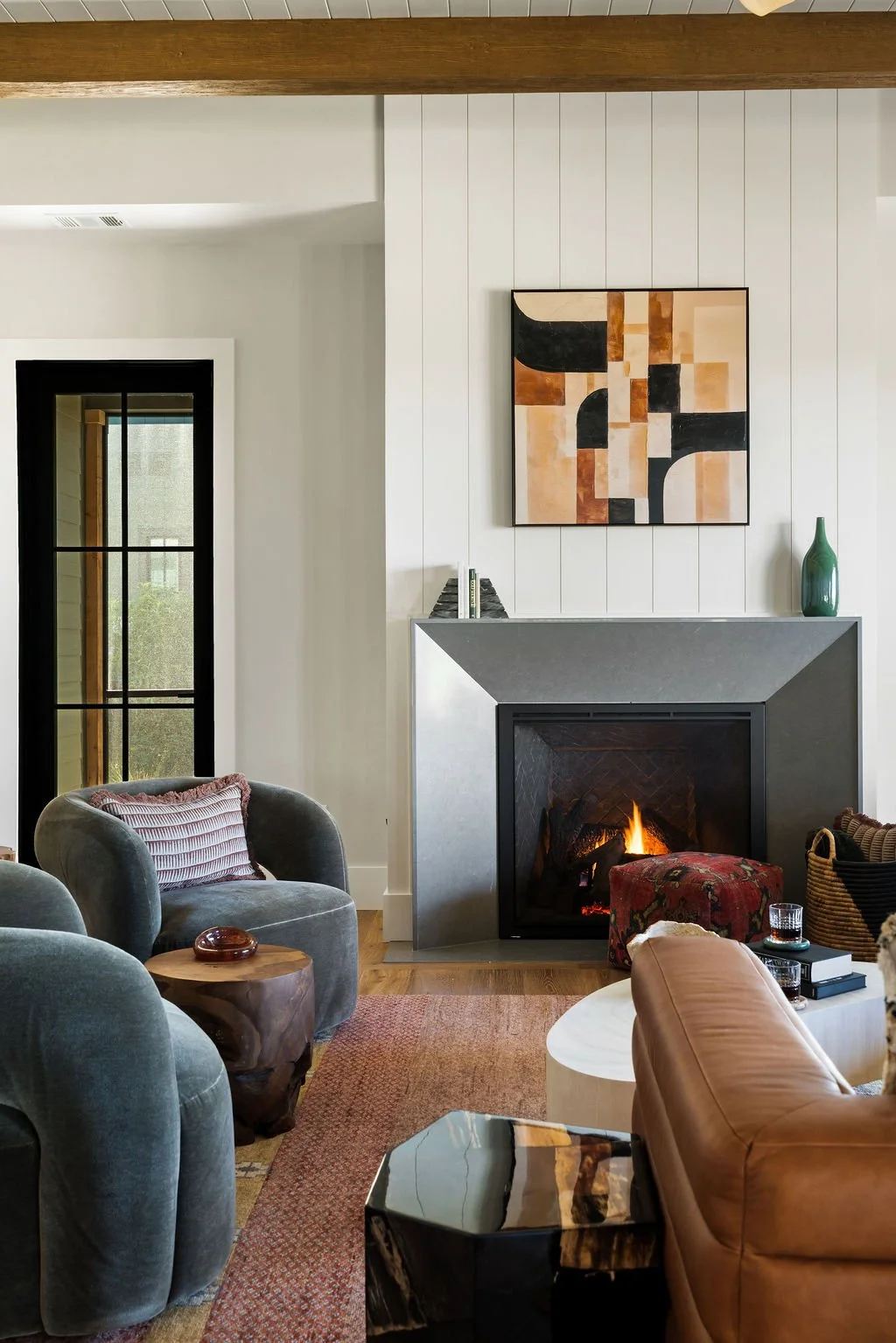 Interior design shot of living room showing leather couch, suede chairs, throw pillow, art, doorway and a fireplace with a slate mantle.